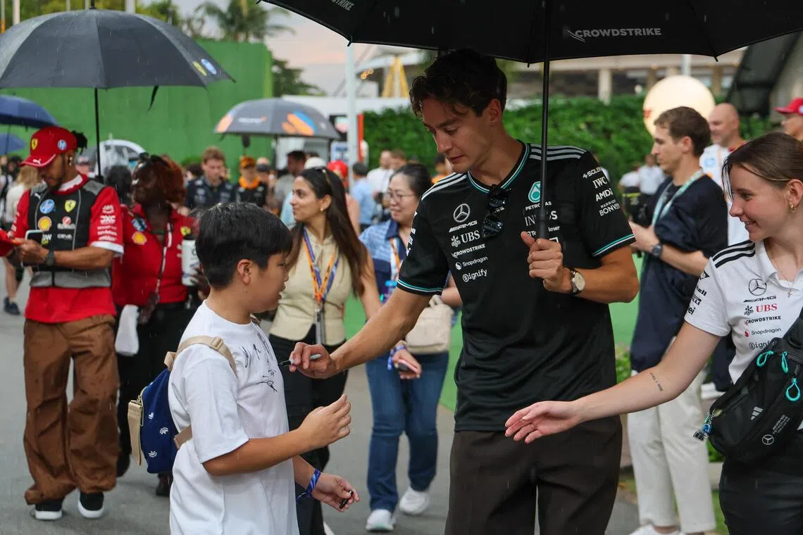 新加坡的大雨也难挡车迷的热情，马赛地车手拉塞尔（右二）星期天在下午为冒雨的小车迷签字留念。（张俊杰摄）