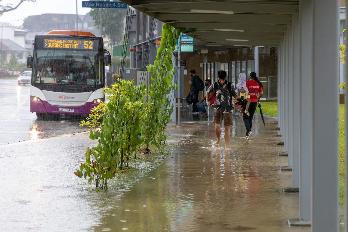汤申路上段的一个巴士站在滂沱大雨后积水，有公众步行时还脱下鞋子，避免鞋子弄湿。（关俊威摄）