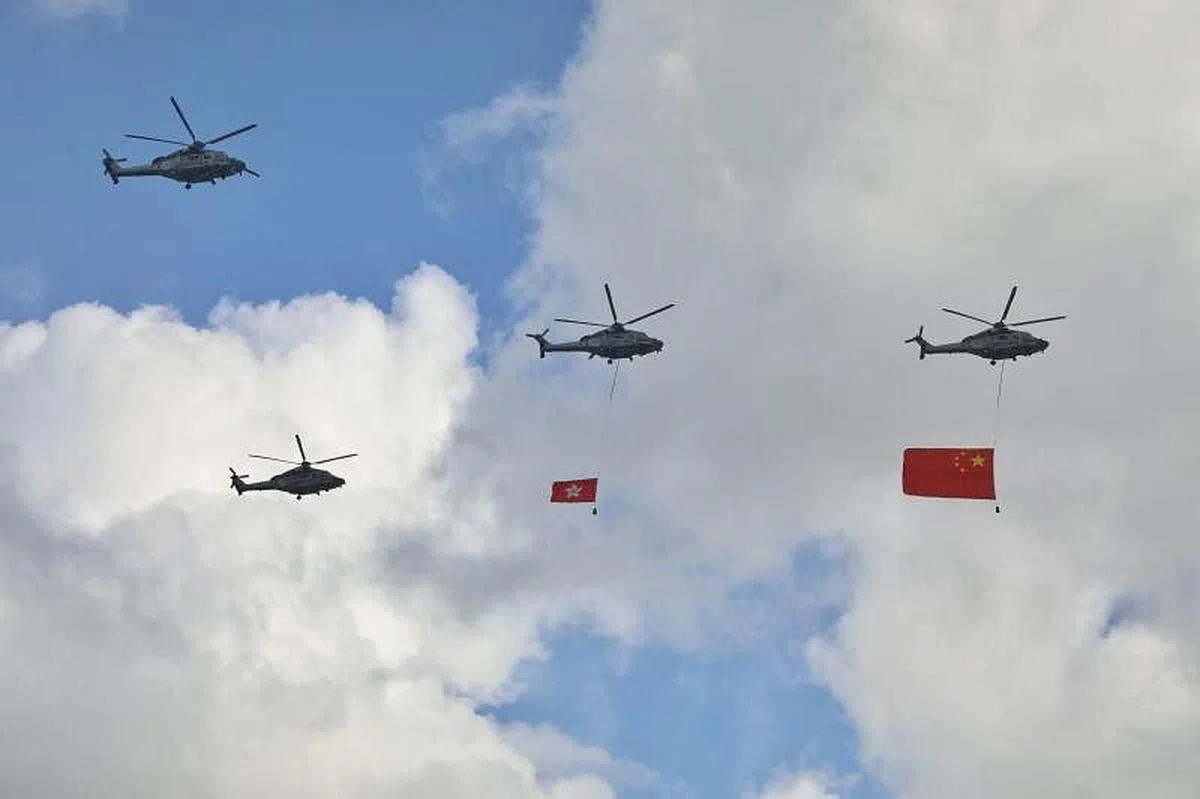 两架直升机分别悬挂着中国国旗和香港区旗飞过维多利亚港上空。（香港中通社） 