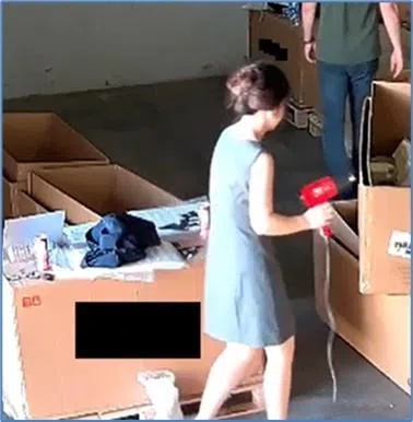 图为“仓库1”一名工作人员用吹风机加热真货包装上的序列号贴纸。（美国司法部官网）