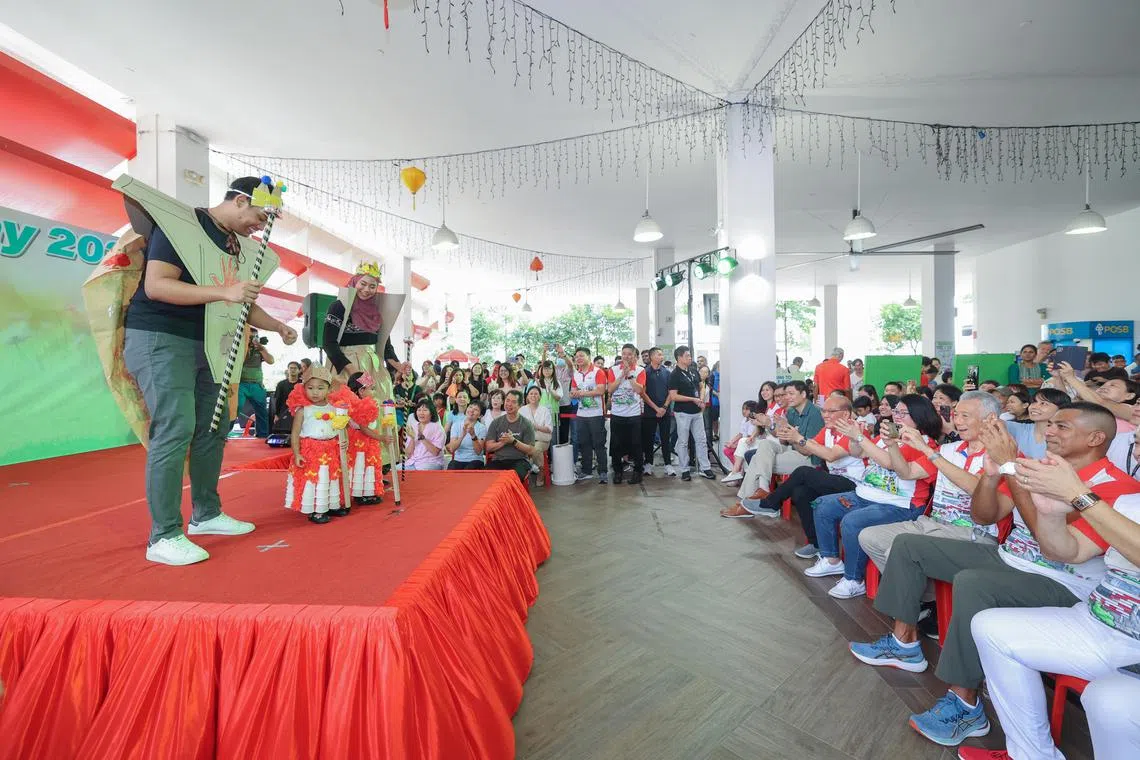 宏茂桥—后港区10个家庭利用废弃材料制作创意服饰，件件别具匠心，赢得在场观众的掌声与欢呼，就连国务资政李显龙（右二）也频频举起手机拍照。台上的哈米赞（左一）一家以皇室为主题，搭配纸皮王冠和权杖。（吴先邦摄）