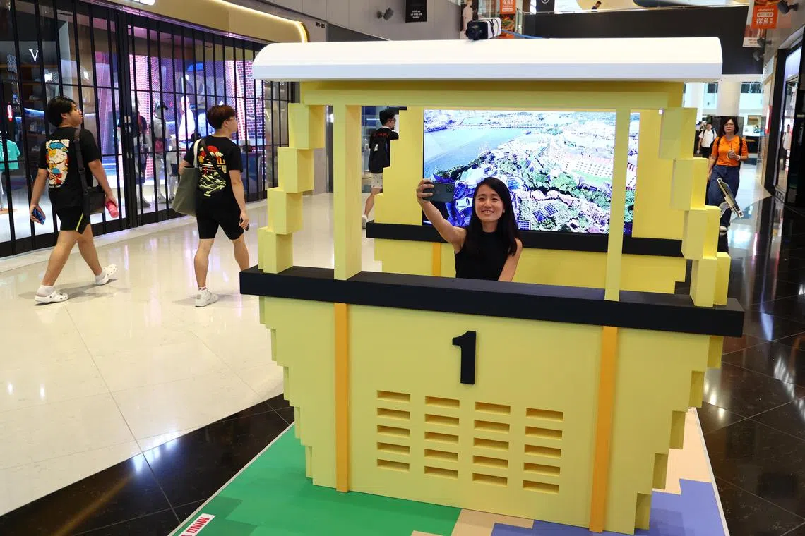 展区的一端，设有以本地首部缆车为模型的电子照相亭。公众可通过平板电脑选择背景图，如1960年代的花柏山或现代的圣淘沙，然后在缆车模型里拍照打卡。（林明顺摄）