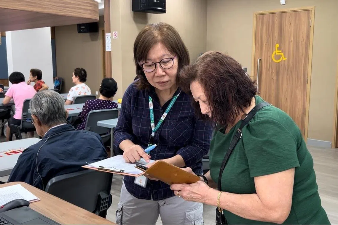 飞跃活跃乐龄中心义工兼会员郑美珍（左），教导会员用手机扫描签到参加手工班。（受访者提供）
