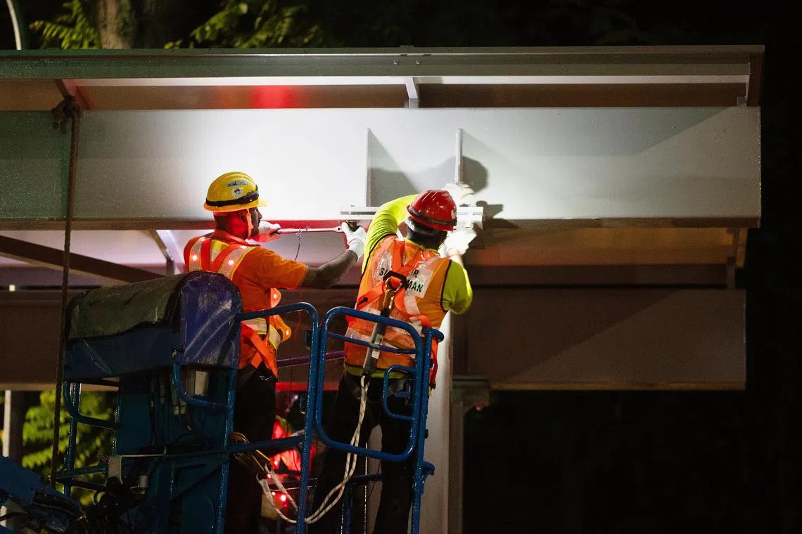 工人站在曲臂升降机上，将屋顶结构螺栓固定在支柱上。（蔡家增摄）