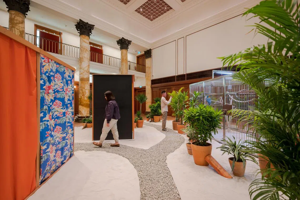 互动式装置艺术《热带》以砾石沙地、热带植物、鹦鹉与木屋等元素，回应对拉美的刻板印象，也希望突破美术馆的高冷氛围，鼓励访客参与其中。（新加坡国家美术馆提供）