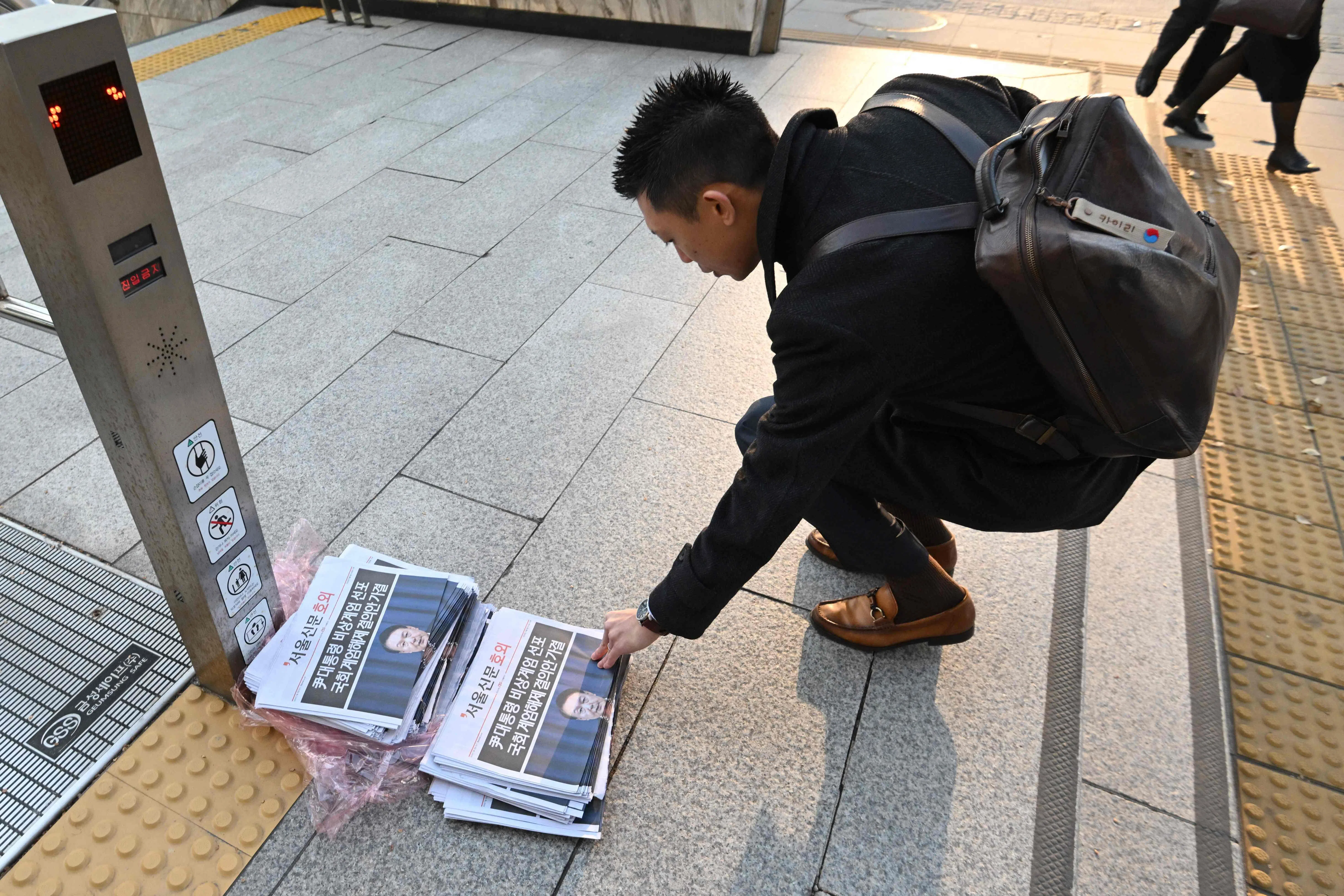 韩国首尔一名男子星期三（12月4日）早上在地铁站出口拿起一份报道总统尹锡悦宣布撤销戒严令的号外。（法新社）