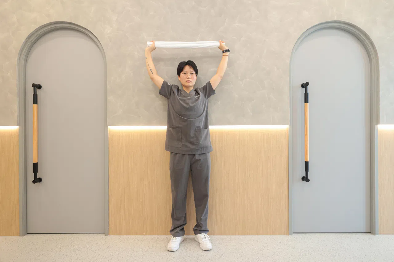 双手握住毛巾两端，双臂向上伸展举高。（李冠卫摄）