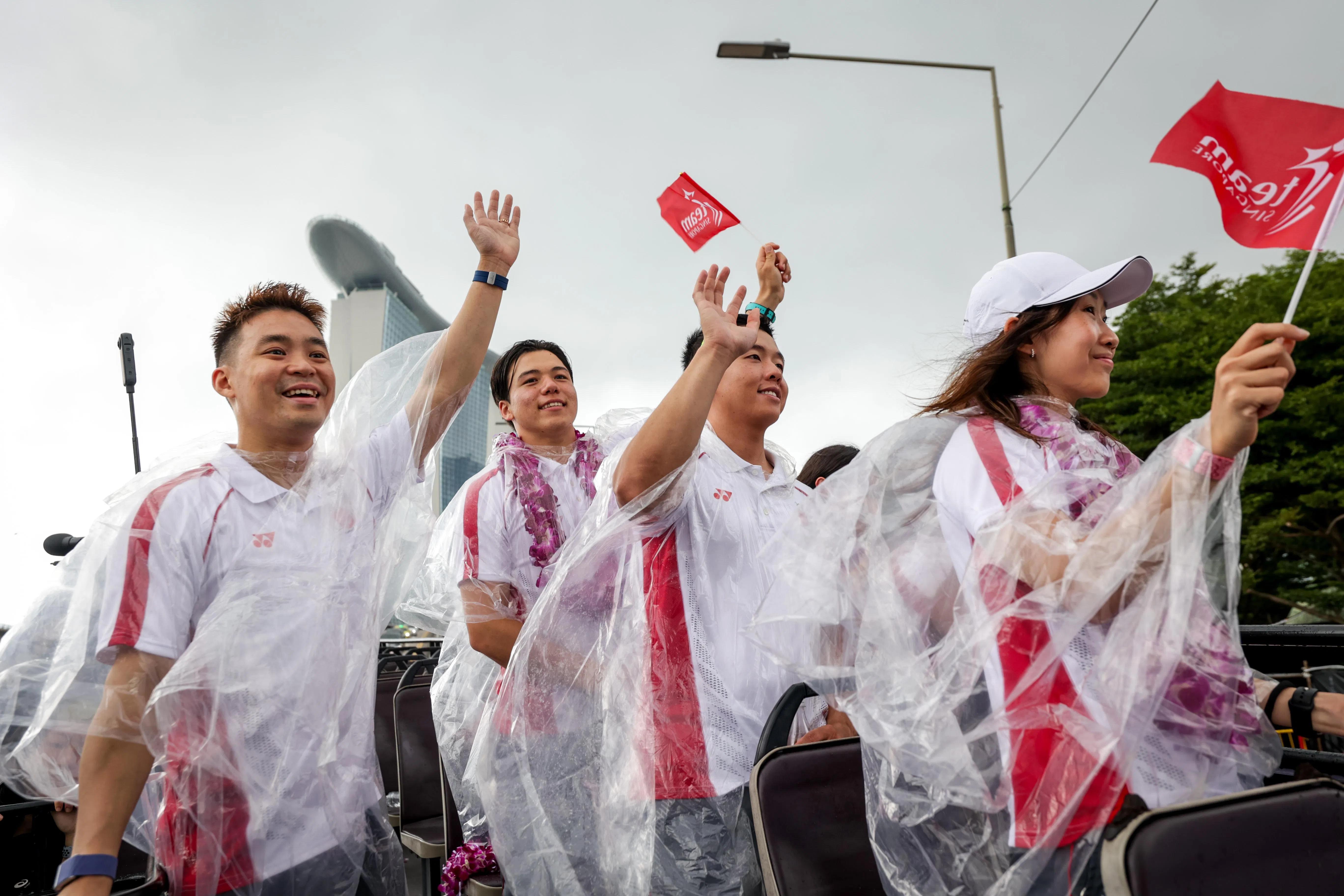我国健儿穿着雨衣，向路边的民众挥手致意，左起为许永凯（羽毛球混双）、墨士廉（水翼风筝板）、卢军汉（男子标准激光级帆船）和陈薇涵（羽毛球混双）。（叶振忠摄）