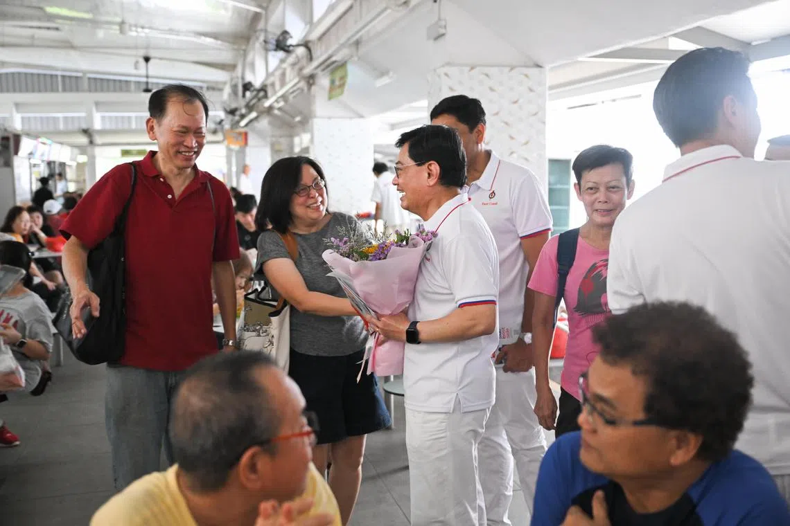 已经宣布引退的王瑞杰副总理（左三站立者），为人民行动党东海岸竞选团队拉票，有居民献花感谢他的照顾与协助。（海峡时报）