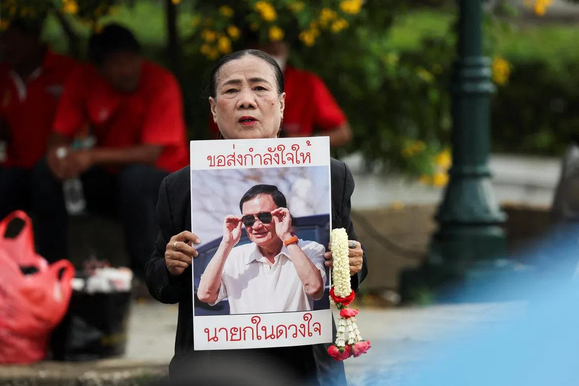 在泰国最高法院外，一名支持达信的妇女手举印有达信照片的海报。（路透社）