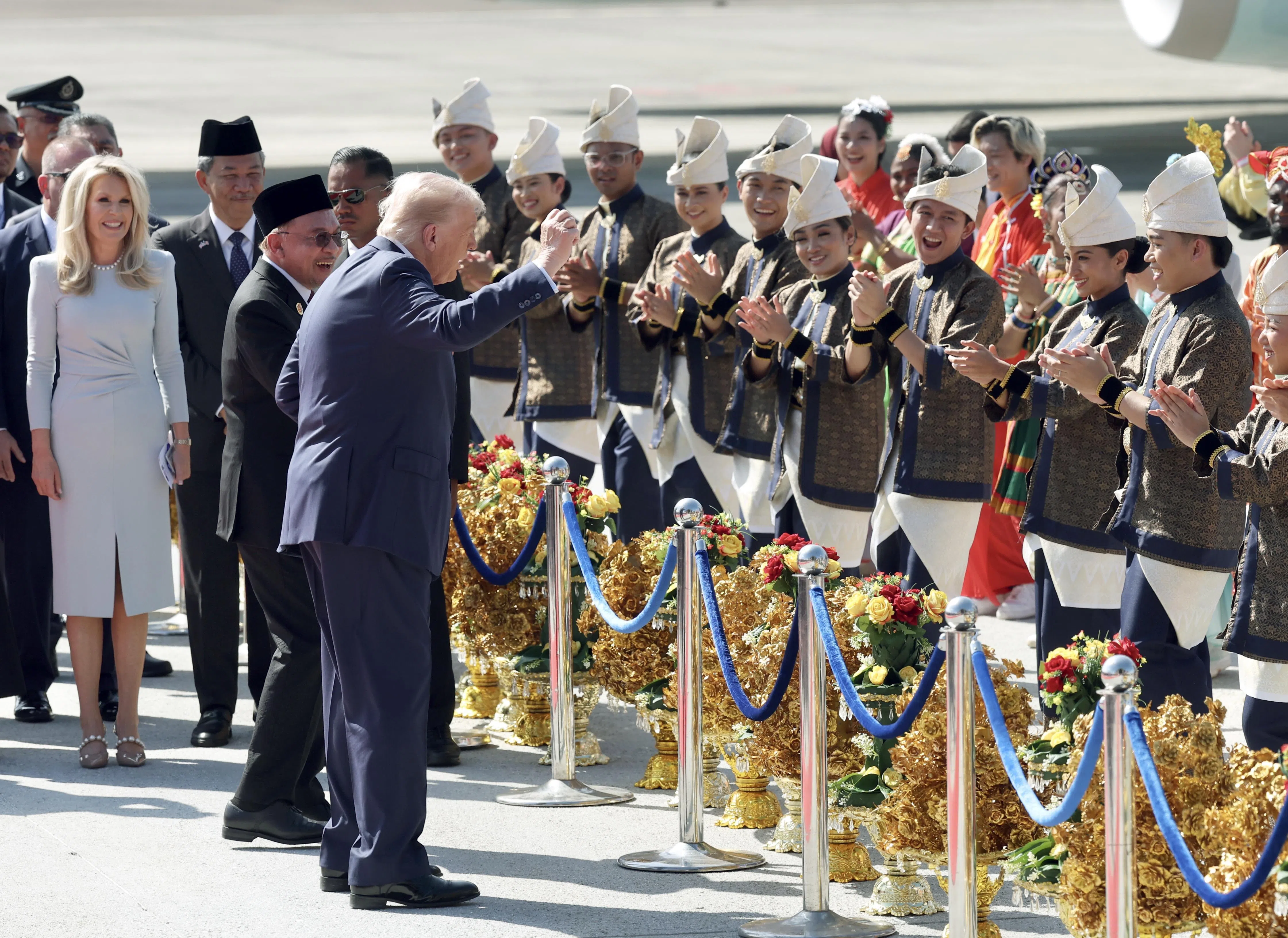 美国总统特朗普（中）星期天（10月26日）飞抵吉隆坡机场，随着欢迎列队的伴舞团手舞足蹈。到场接机的马来西亚首相安华（特朗普左侧）也跟着摆动起双手，笑得合不拢嘴。（马新社）