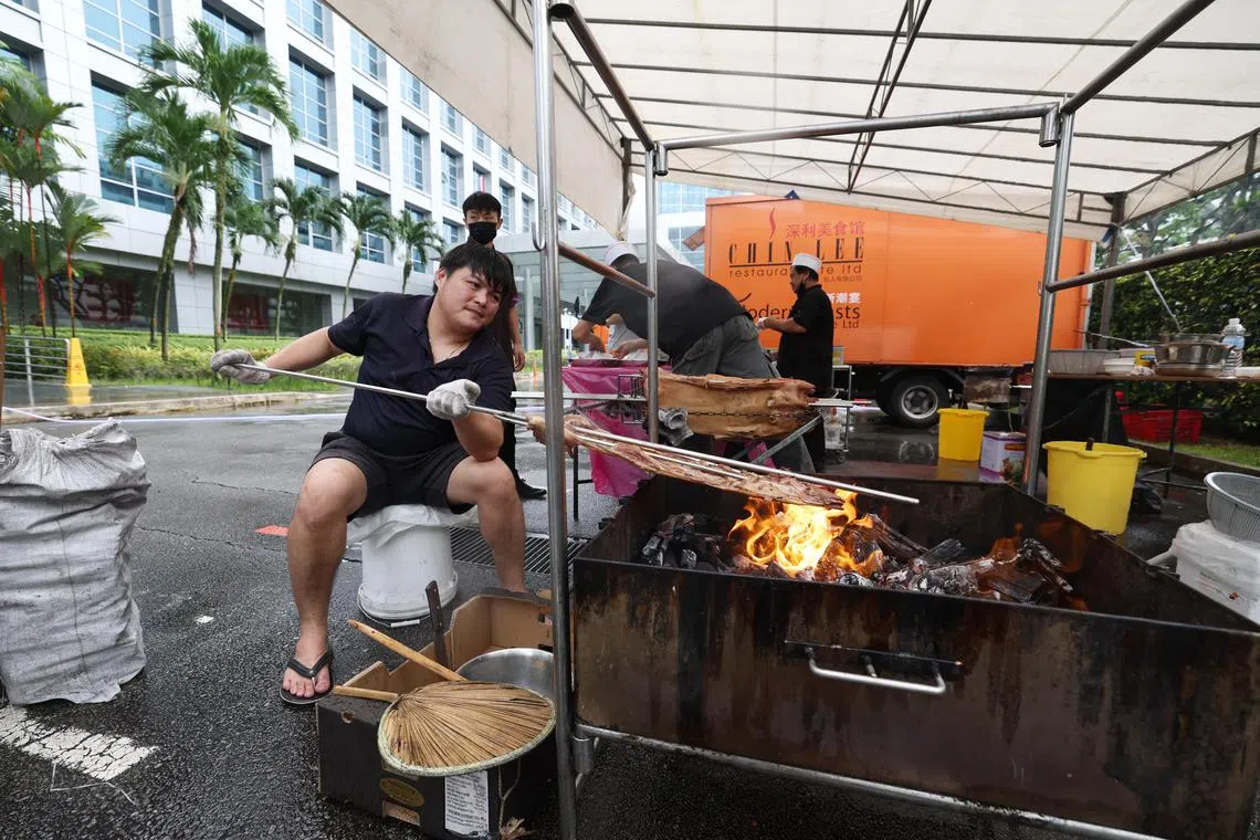 潮州餐馆深利美食馆为星期天的早报专栏作者交流会提供午餐。图为餐馆人员在报业中心礼堂外设置帐篷烘烤乳猪。（陈渊庄摄）