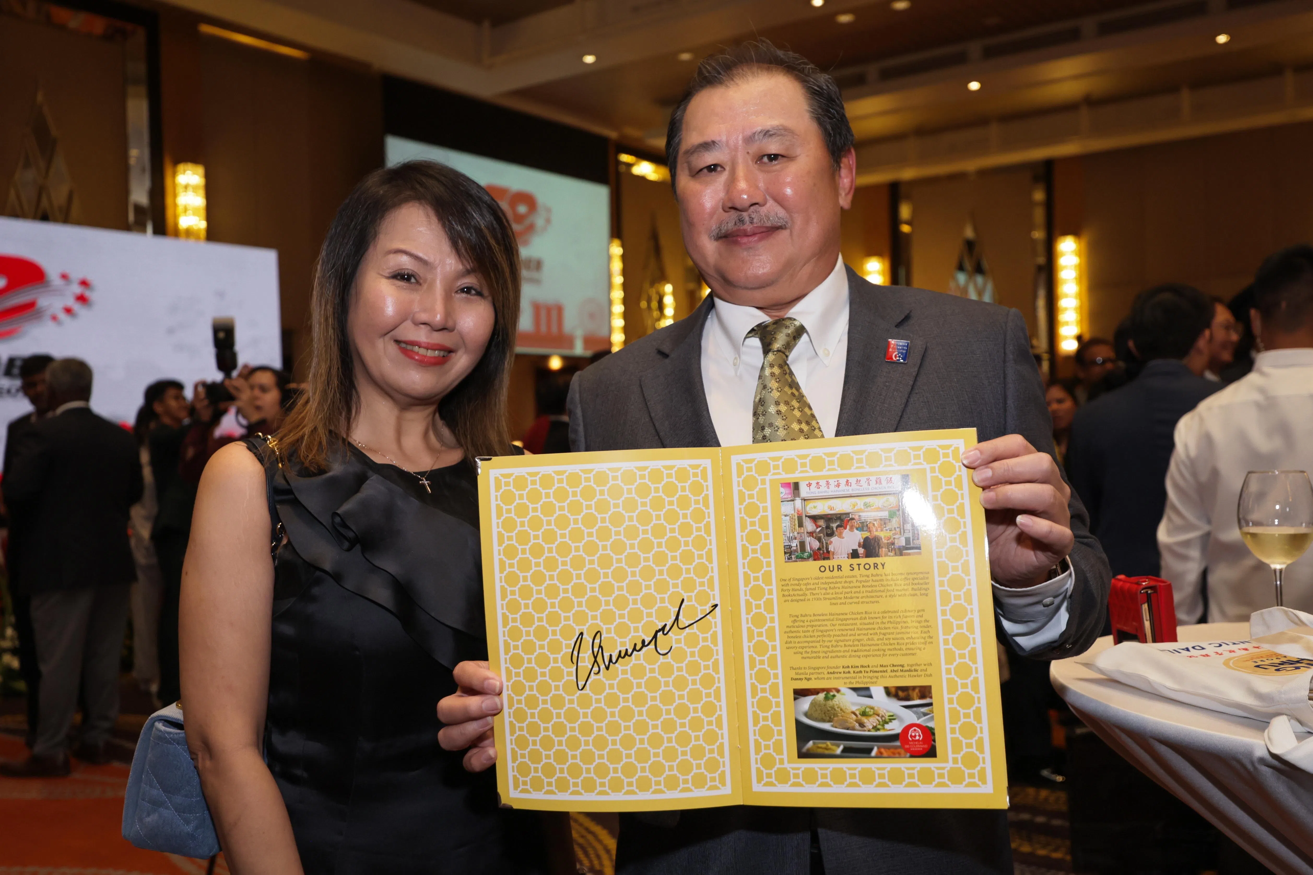在菲律宾马尼拉开设了12家“中峇鲁起骨海南鸡饭”餐馆分行的许文勇（右）和妻子吴玉英，星期五与尚达曼总统见面时，请他在餐馆菜单上签名。（海峡时报）