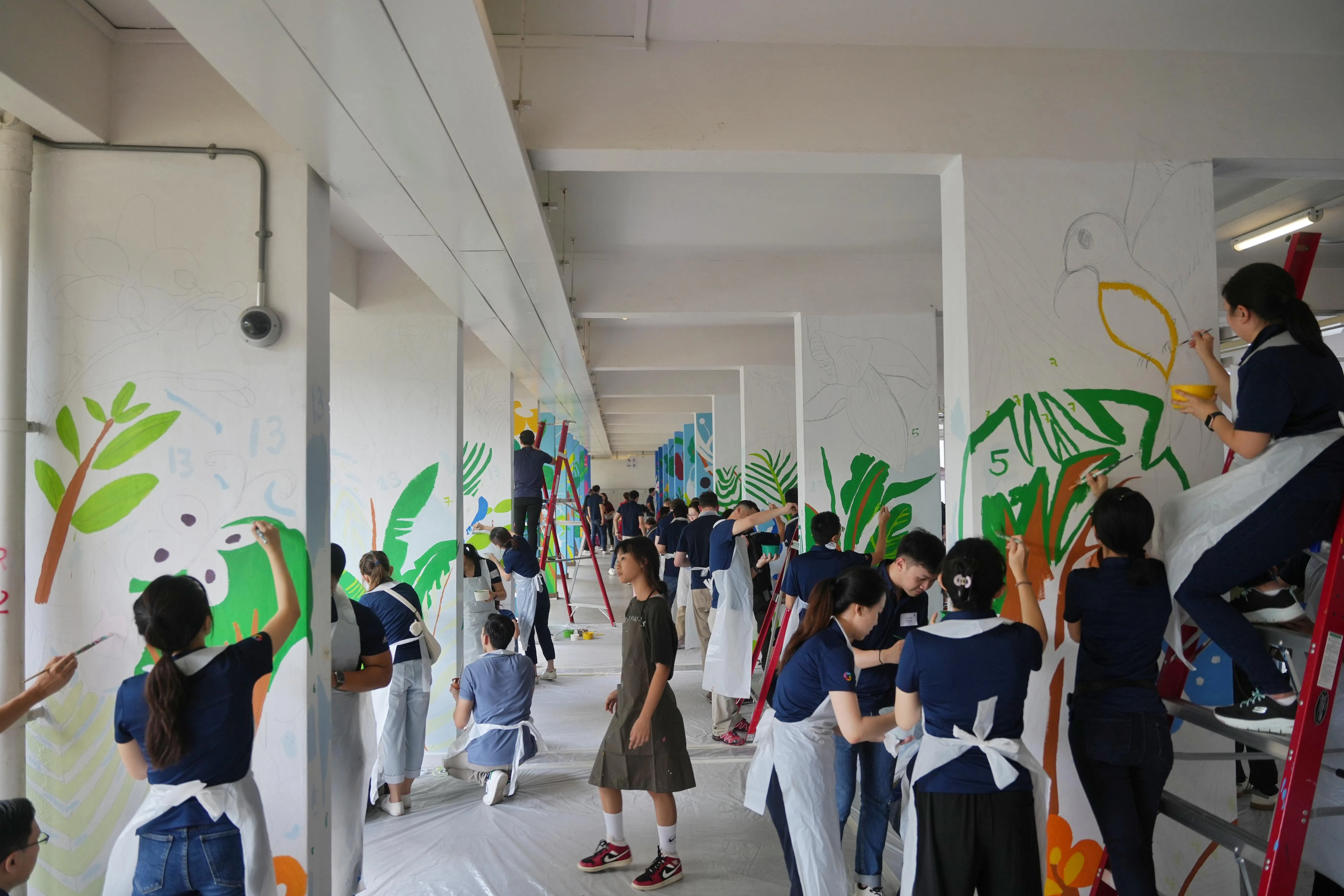 来自淡马锡的义工和天猛公艺术基金会的艺术家齐心协力为壁画上色。壁画中一些植物和鸟儿的图案，来自特需学生的设计。（谢智扬摄）