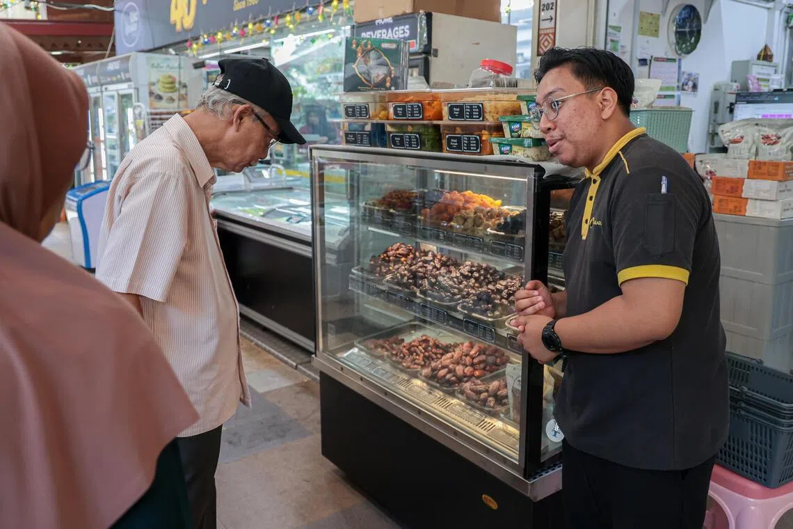 AL Barakah店员伊尔凡（右一）正在为顾客介绍从伊朗、沙特阿拉伯、约旦等国进口的各类蜜枣和干果。（李冠卫摄）