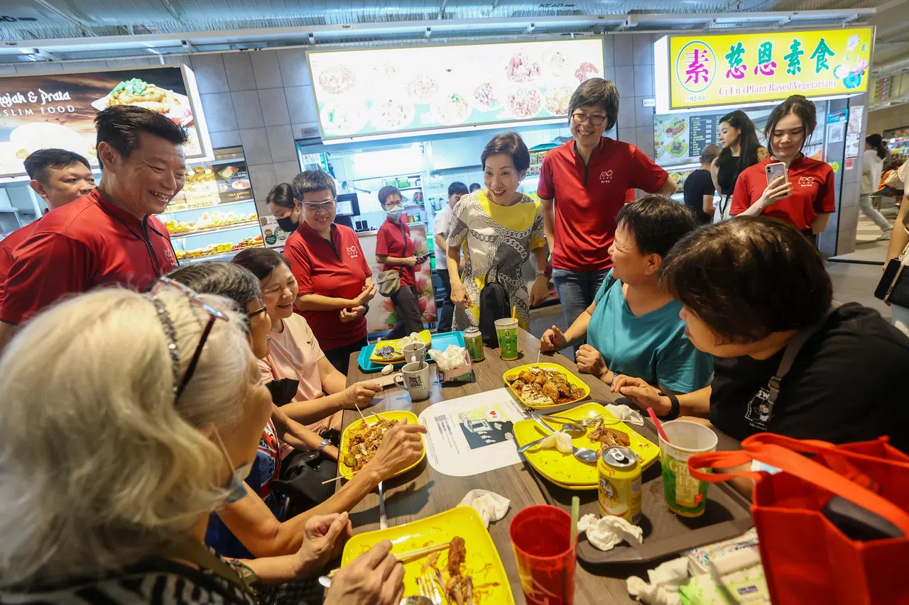 永续发展与环境部长傅海燕（左三）与《联合早报》总编辑吴新迪（左起红衣者）、执行总编辑韩咏梅和新报业媒体华文媒体集团社长李慧玲，在榜鹅综合社区中心小贩中心，向食客推荐漫画展。（陈渊庄摄）