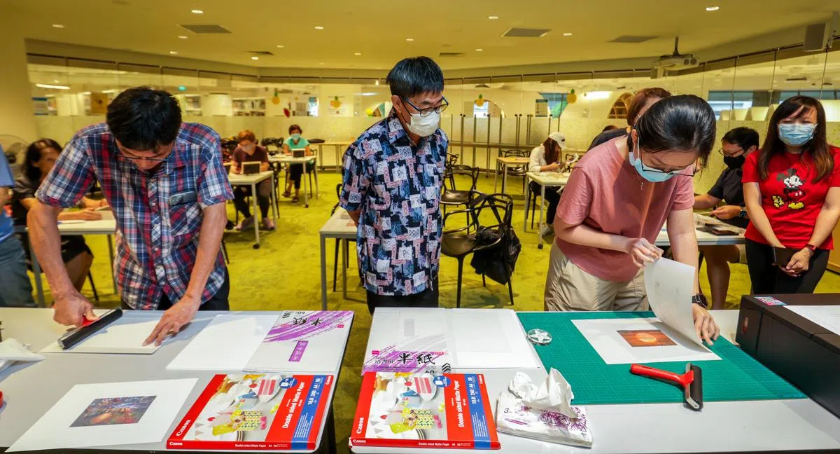 工作坊参与者将蜡纸印有照片的一面压在宣纸上，再用滚轴来回滚动蜡纸，将图像的油墨转移到宣纸上。（叶振忠摄）