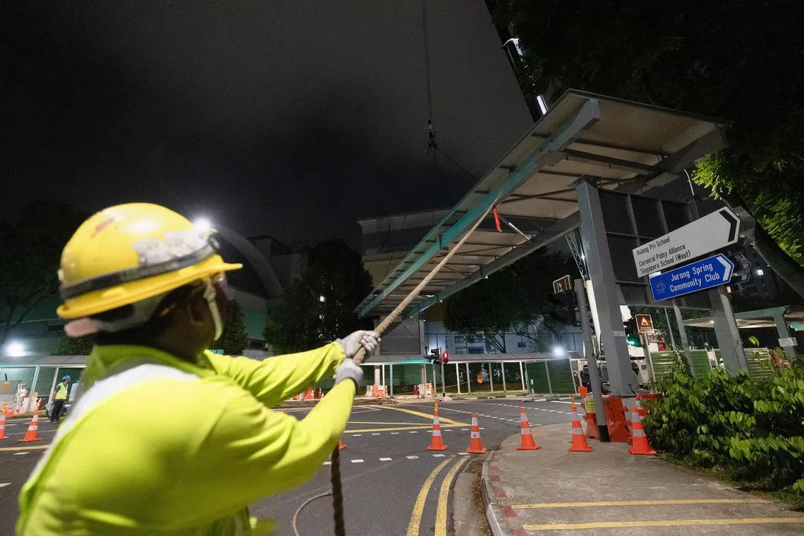 工人使用两条斜拉的绳索协助引导结构入位，随后将它固定在道路两侧的支柱上。（蔡家增摄）