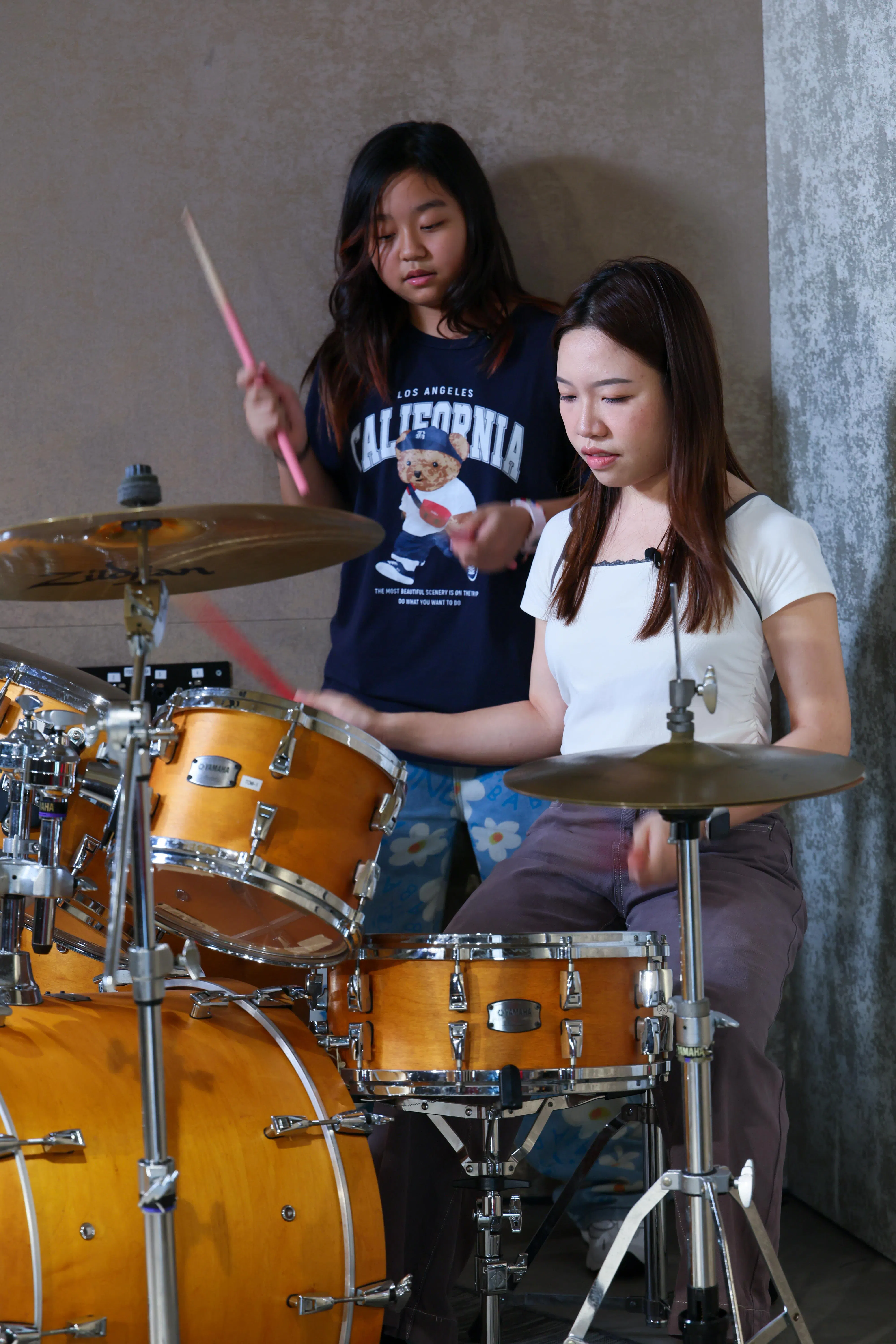 黄姿宁（左）化身音乐老师，教毫无基础的记者打鼓。（龙国雄摄）