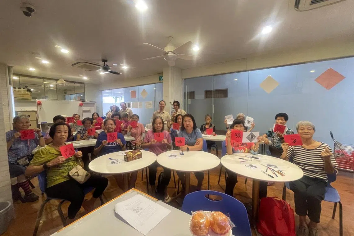宏茂桥4道第257座组屋的太和观活跃乐龄中心的长者展现他们在现场画出的新年红纸，与华中学生合影。（作者提供）
