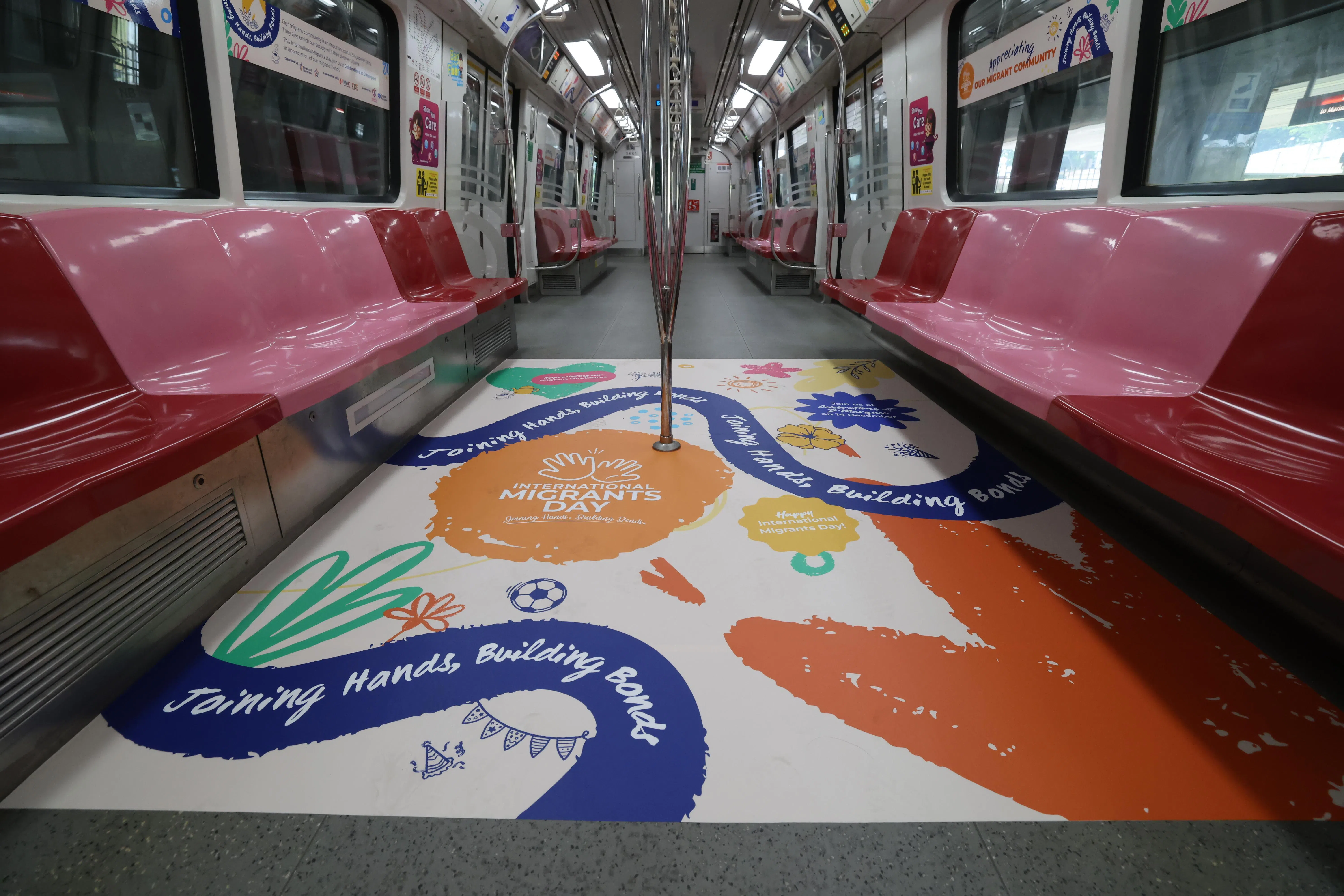 “国际客工日”地铁概念列车川行于东西线和南北线，列车地板布置印有“携手建立纽带”等英文短语的图饰，鼓励乘客向客工传达谢意。（梁麒麟摄）