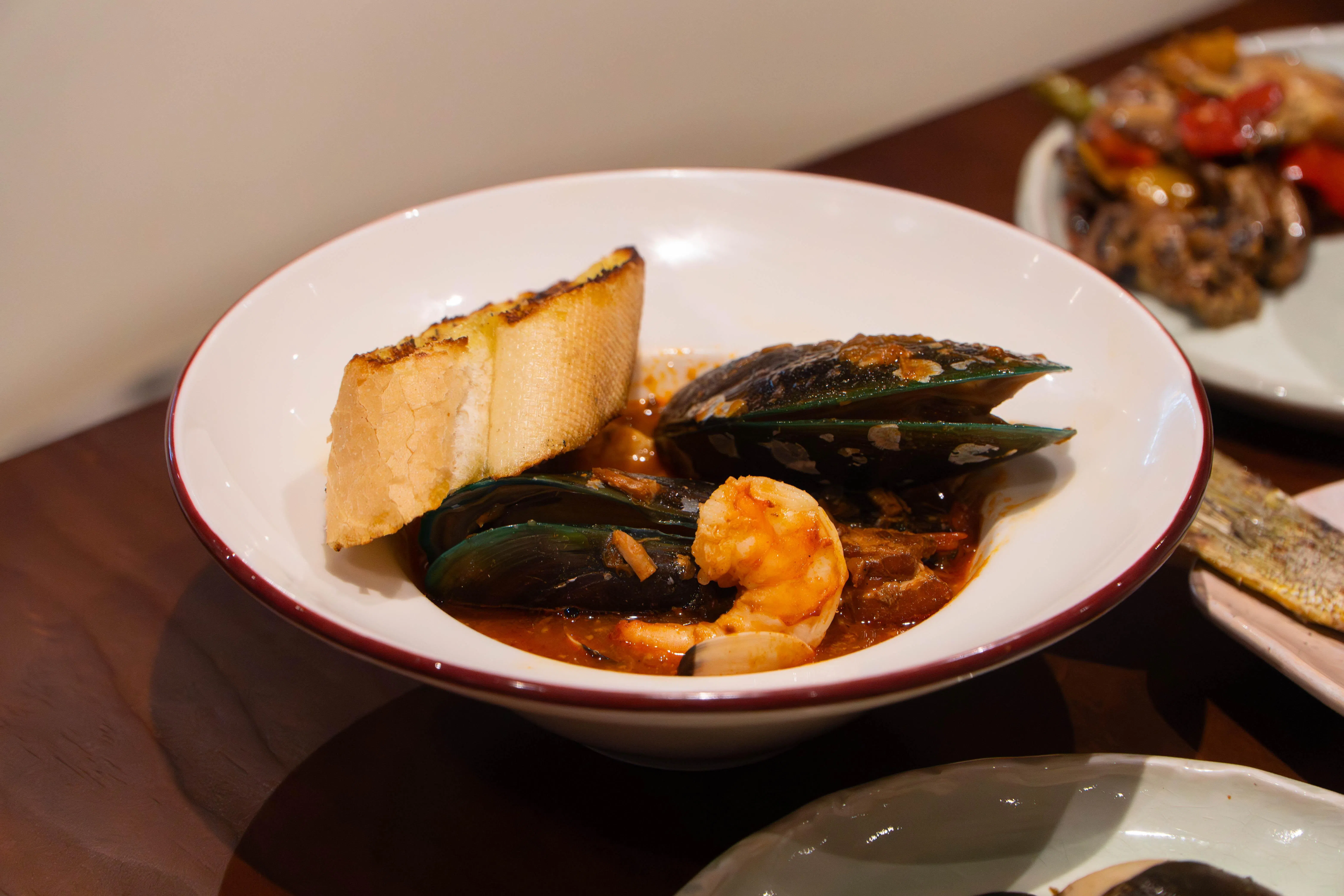 葡式海鲜炖菜包含青口贝、蛤蜊、虾与猪五花等，在浓郁番茄酱汁中慢炖入味，搭配烤蒜香面包享用。（餐馆提供）