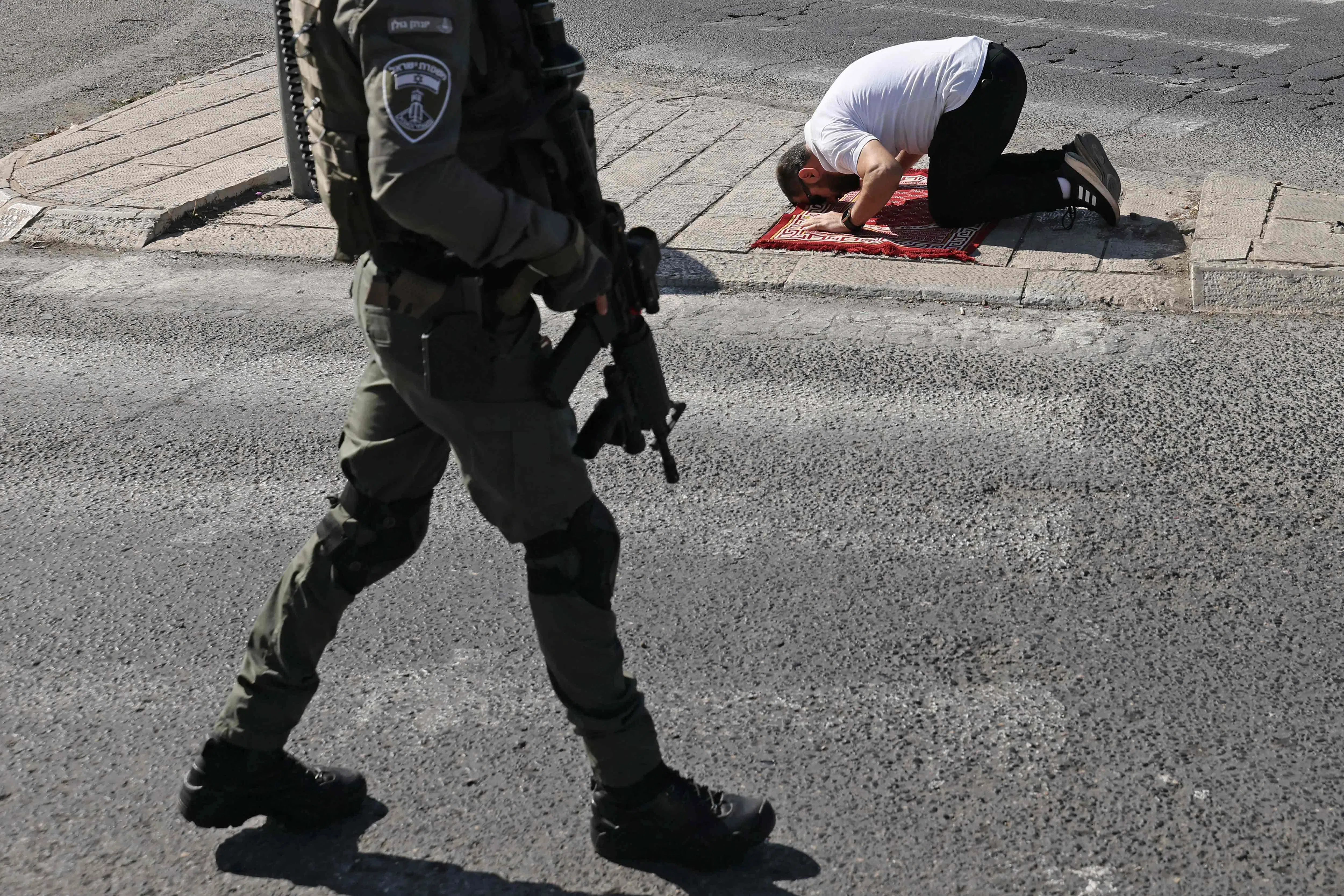 11月10日，一名男子在东耶路撒冷的拉斯阿穆德（Ras al-Amud）社区的马路上，不顾一旁持枪巡逻的以色列安全人员，进行午时祈祷。（法新社）
