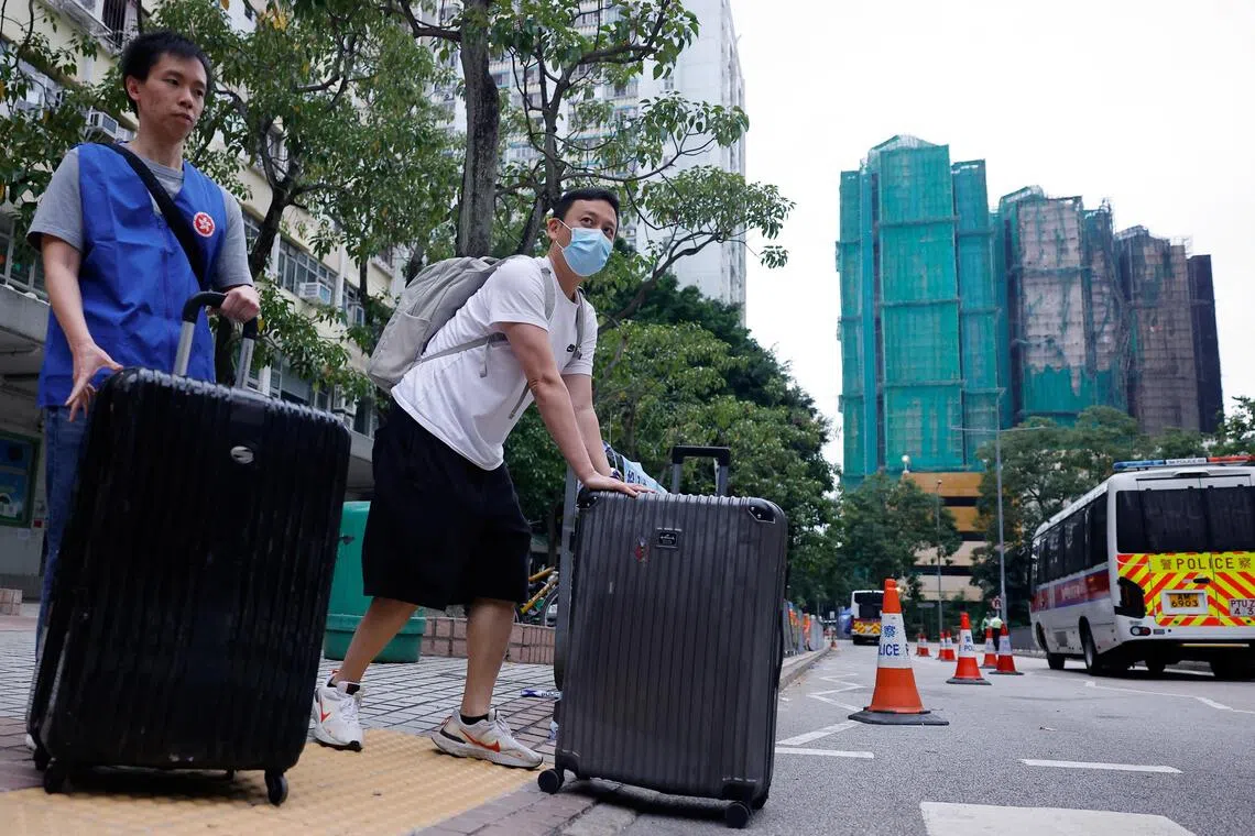 未受大火波及的宏志阁（背景中全栋覆盖了绿色棚网的大楼）居民（右）星期三（12月3日）回家取回个人物品后和志愿者推着行李箱离开。（路透社）