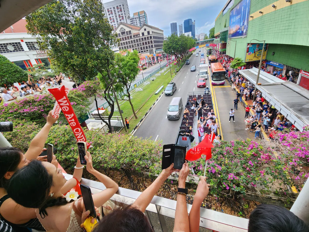 巴士经过牛车水时，不少民众在路旁和天桥上迎接我国健儿。（何家俊摄）