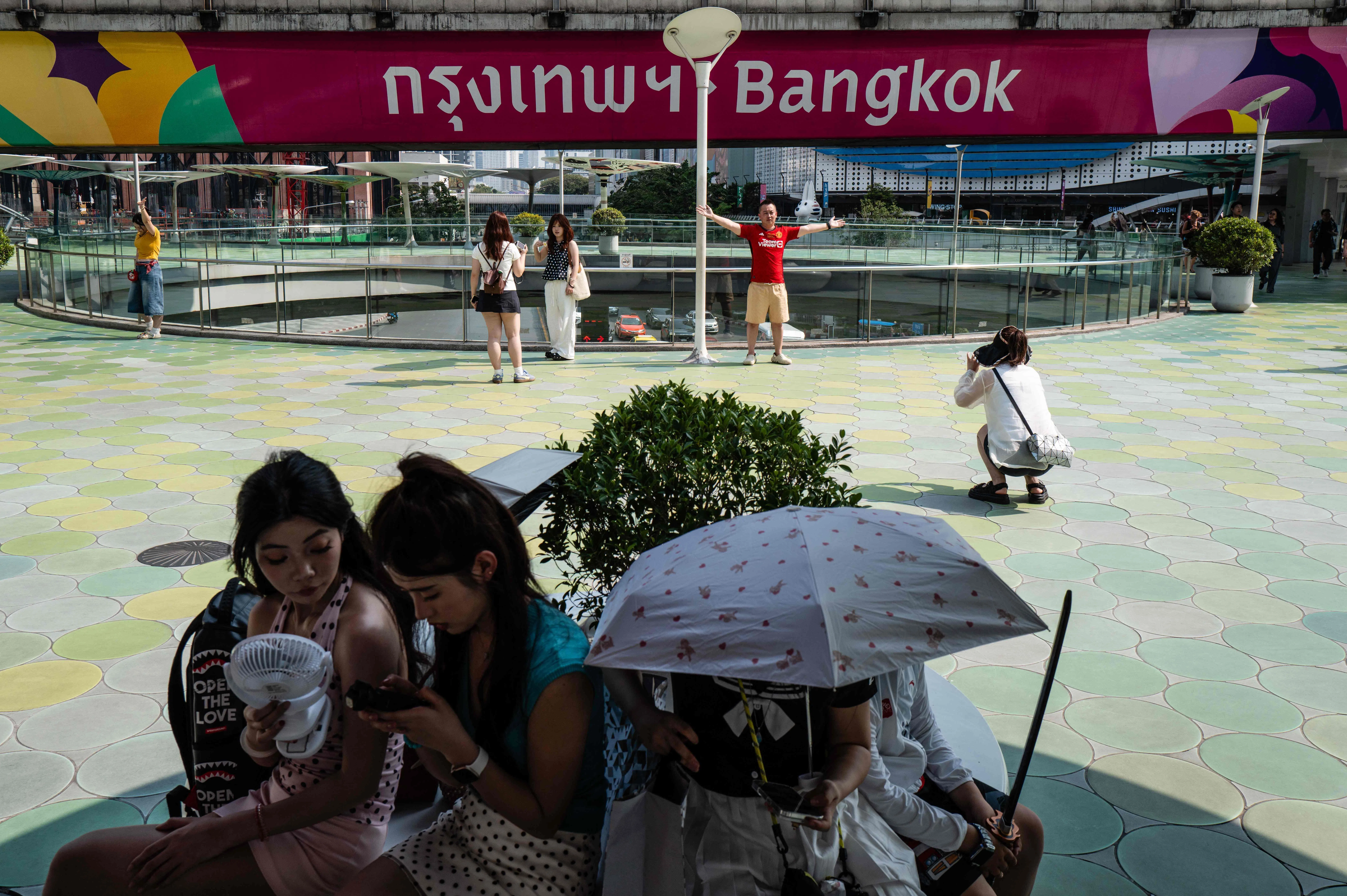 泰国首都曼谷近日天气酷热难耐，人们在户外都撑伞遮阴，或随身携带及使用便携式风扇降温。（法新社）