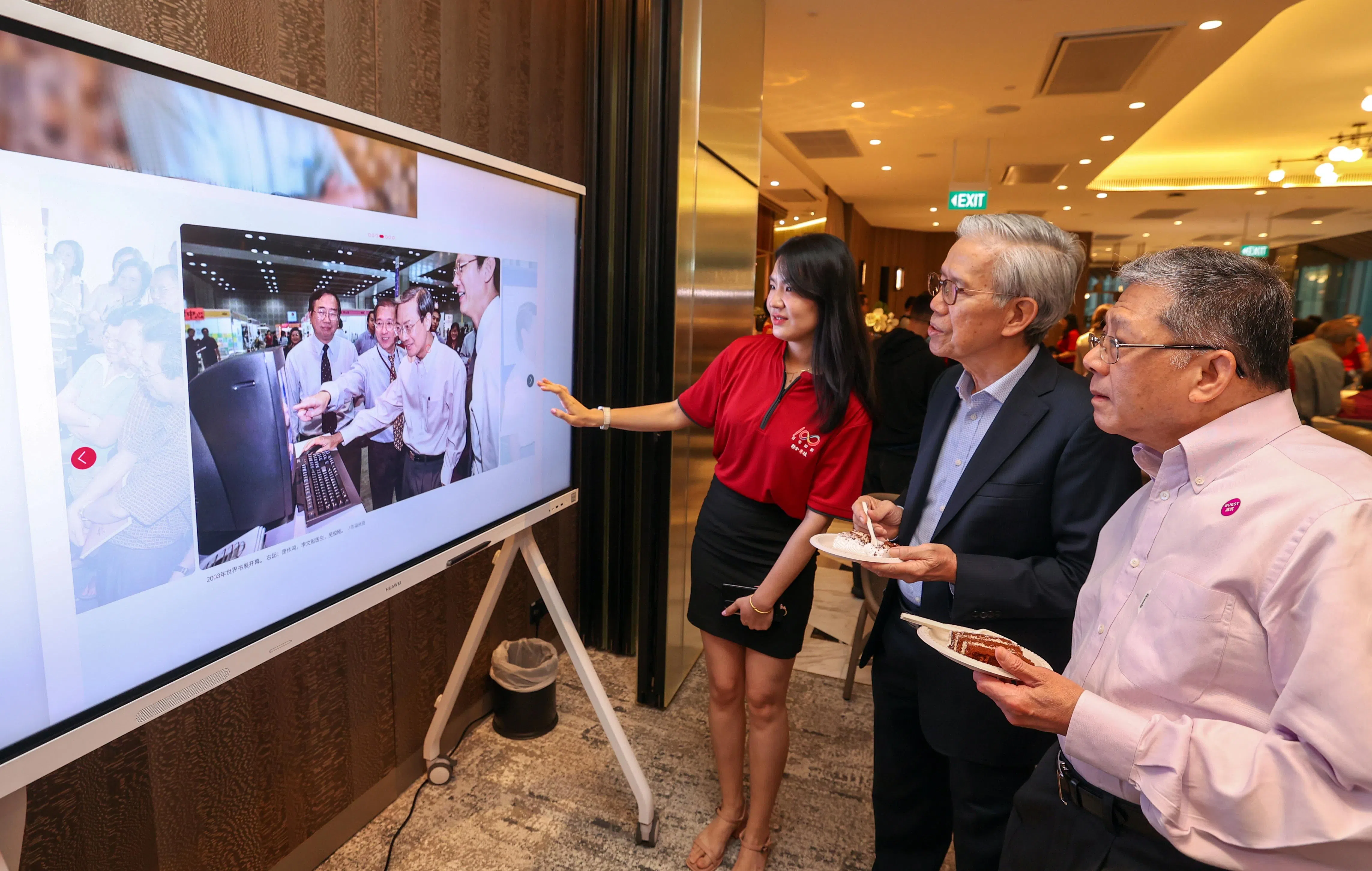《联合早报》在庆生会上，通过大型智能屏幕向嘉宾展示各个项目的精彩内容。图为早报客制企划组视频编导王瑶（左起）向怡和轩主席胡财辉和亚非大厦业主陈精毅介绍早报口述历史网站。亚非大厦是早报的前身《南洋商报》旧址。胡财辉是早报百年庆基金的捐赠者。（白艳琳摄）