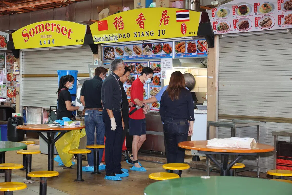 男嫌犯（红衣者）星期二（10月15日）早上在警员押送下，被带返小贩中心重组案情。（唐家鸿摄）