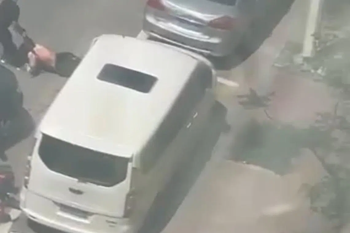 女子躲到停泊在路边的私家车车底，被男司机拉回到路中间。（视频截图）