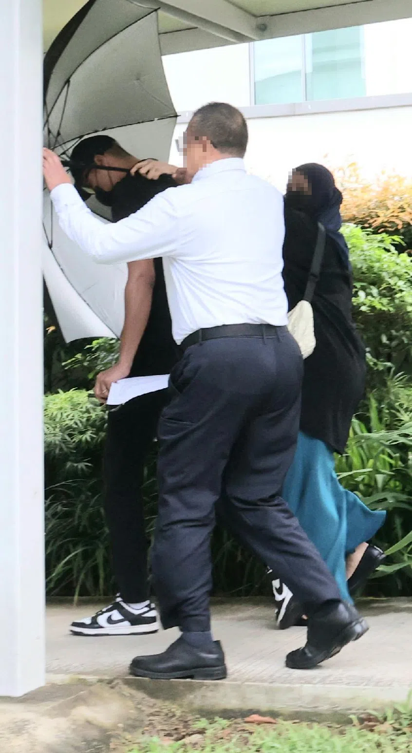 法官批准被告努尔哈基姆（左一）3月1日服刑，被告保释出来后，用雨伞遮着脸，在亲友陪同下走出国家法院。（蔡振鸿摄）