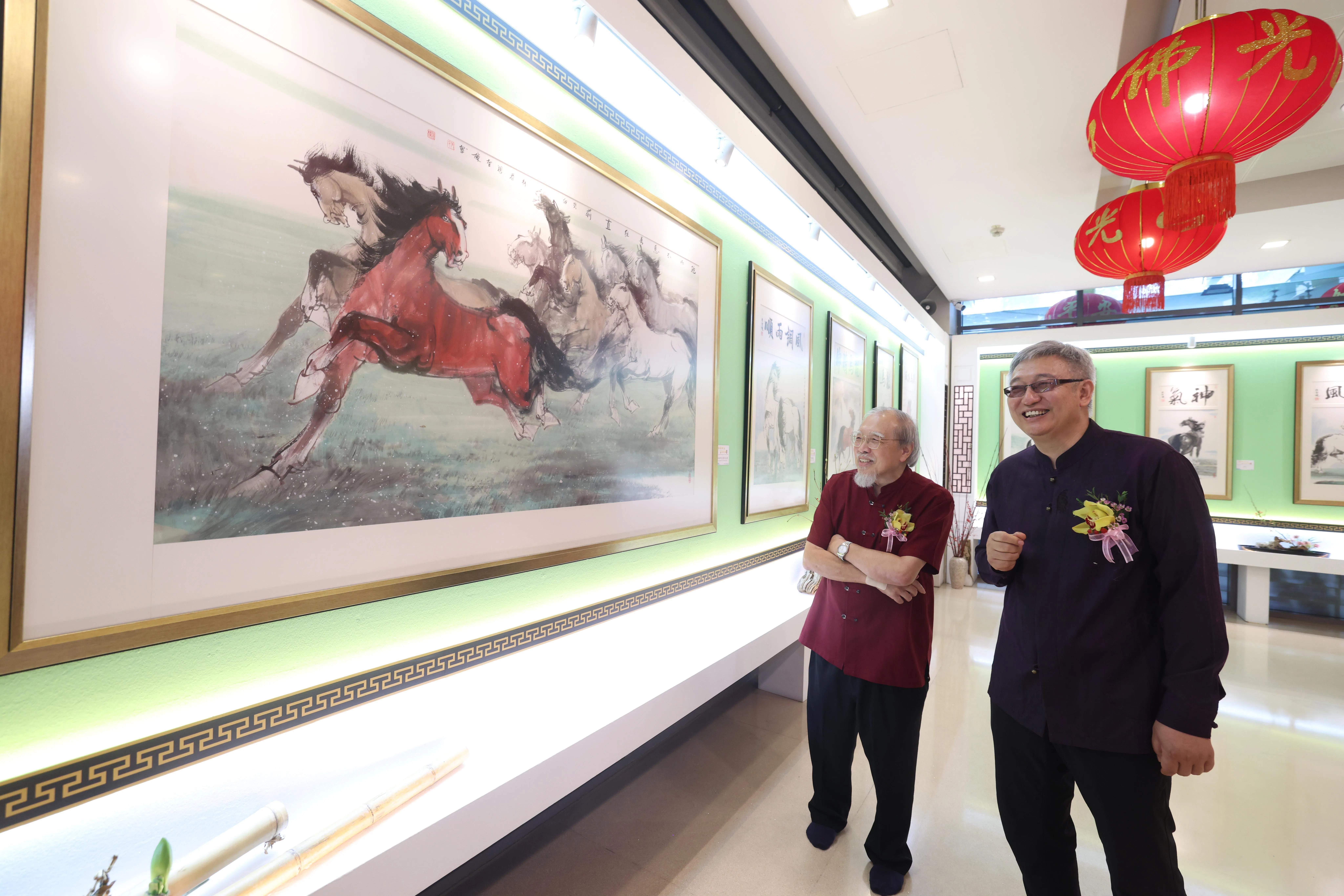 中国画家张智栋（右）的“和谐共生，马到成功”个人画展1月17日至2月28日在新加坡佛光山举行，他在画展开幕礼上向好友梁振康介绍画作《驰而不息勇往直前》。（郑一鸣摄）