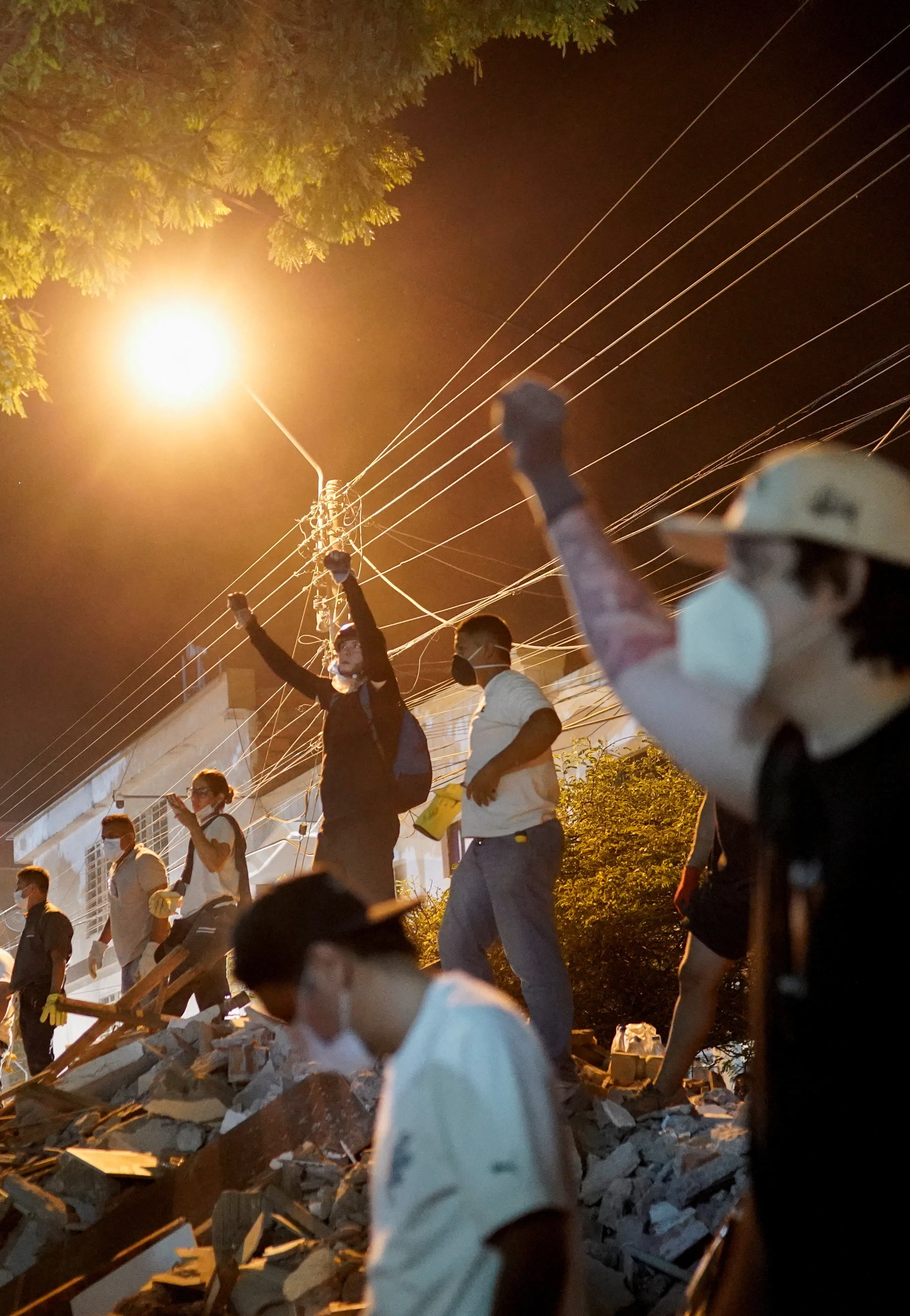 救援人员在夜晚的街灯下双手握拳高举半空，示意现场保持绝对寂静，以捕捉废墟底下发出的哪怕再微弱的生命气息。（路透社）