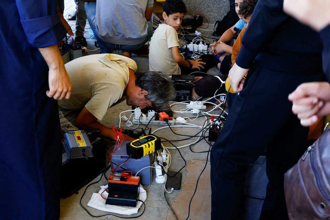 加沙地带的电供在冲突爆发后被切断，当地一家电器店的老板用太阳能板设置充电站，让民众给手机充电。（路透社）