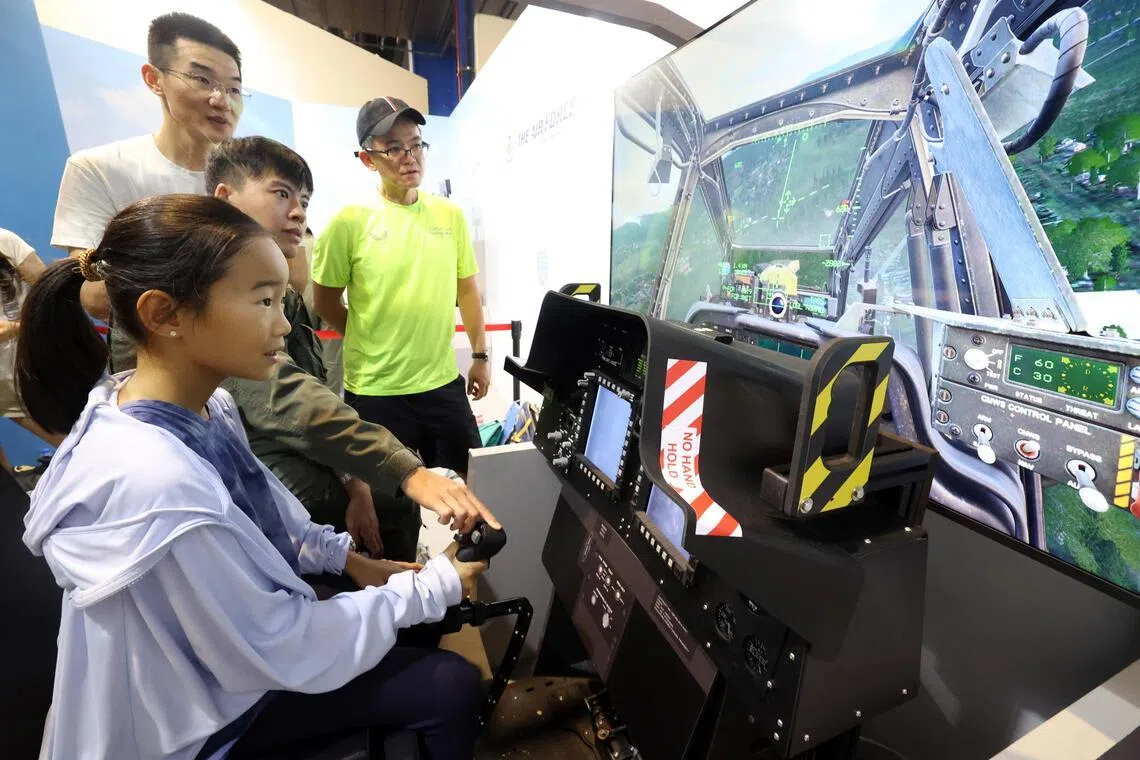 在新加坡空军部队展区，女孩尝试操作AH-64D型阿帕奇攻击直升机模拟器，体验飞行操控。（邝启聪摄）