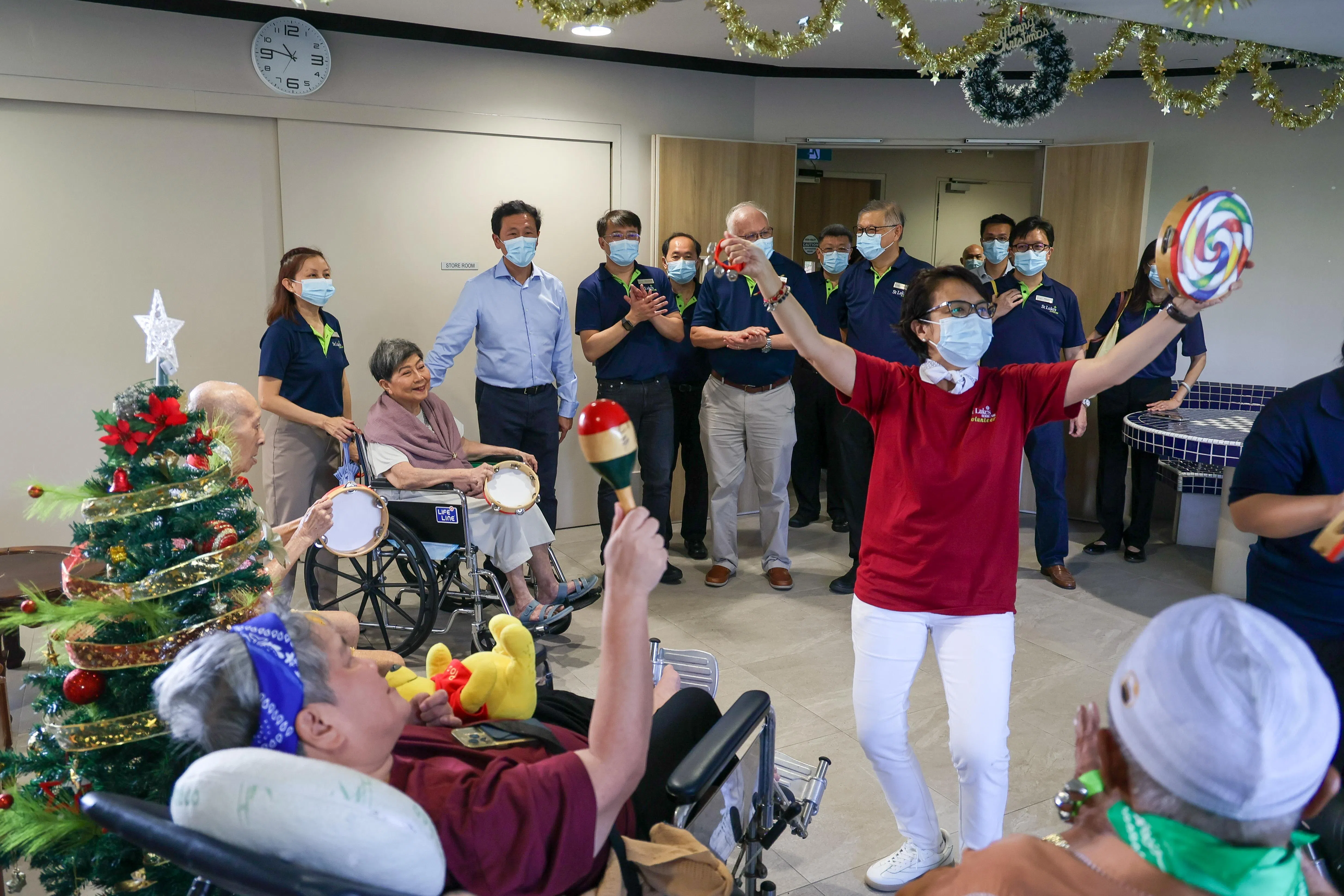 圣路加乐龄关怀星期三（12月10日）庆祝推出疗养院服务五周年，社会政策统筹部长兼卫生部长王乙康（后排左三）是主宾。圣路加乐龄关怀在2020年5月疫情最严重时，在宏茂桥开设第一家疗养院，并运营至今。除了一般照护外，疗养院也为年长者提供一系列文娱活动，包括制作个人回忆录、音乐疗愈活动、心理辅导等。图为失智症老人参与为他们设计的音乐互动节目。（张俊杰摄）