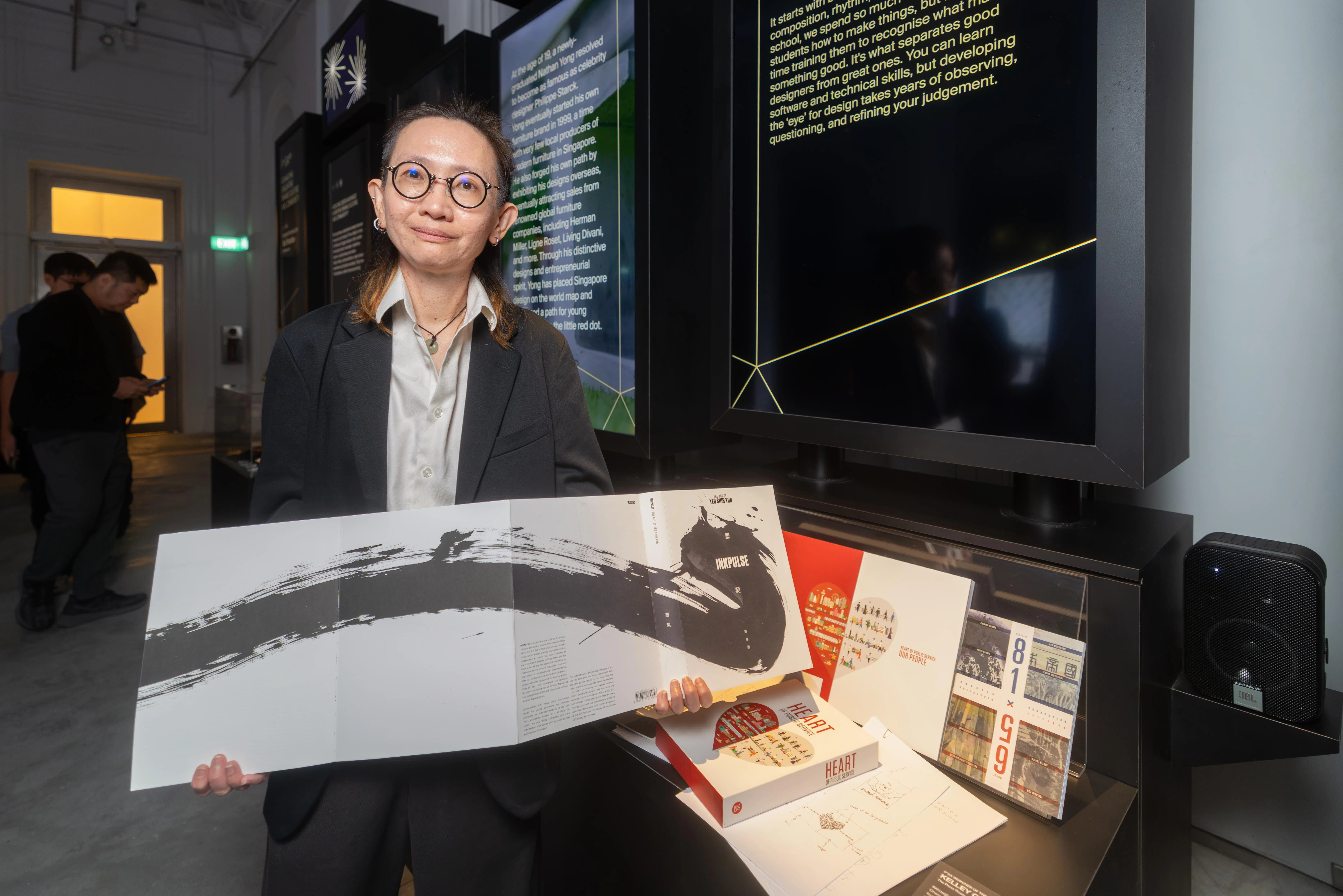 钟瑞林展示她为当代水墨艺术家姚诗韵设计的回顾展画册《墨契》；桌上摆着的红白合拼为心的图册，则是她为总理公署所设计的《公共服务的心》。（吴先邦摄）