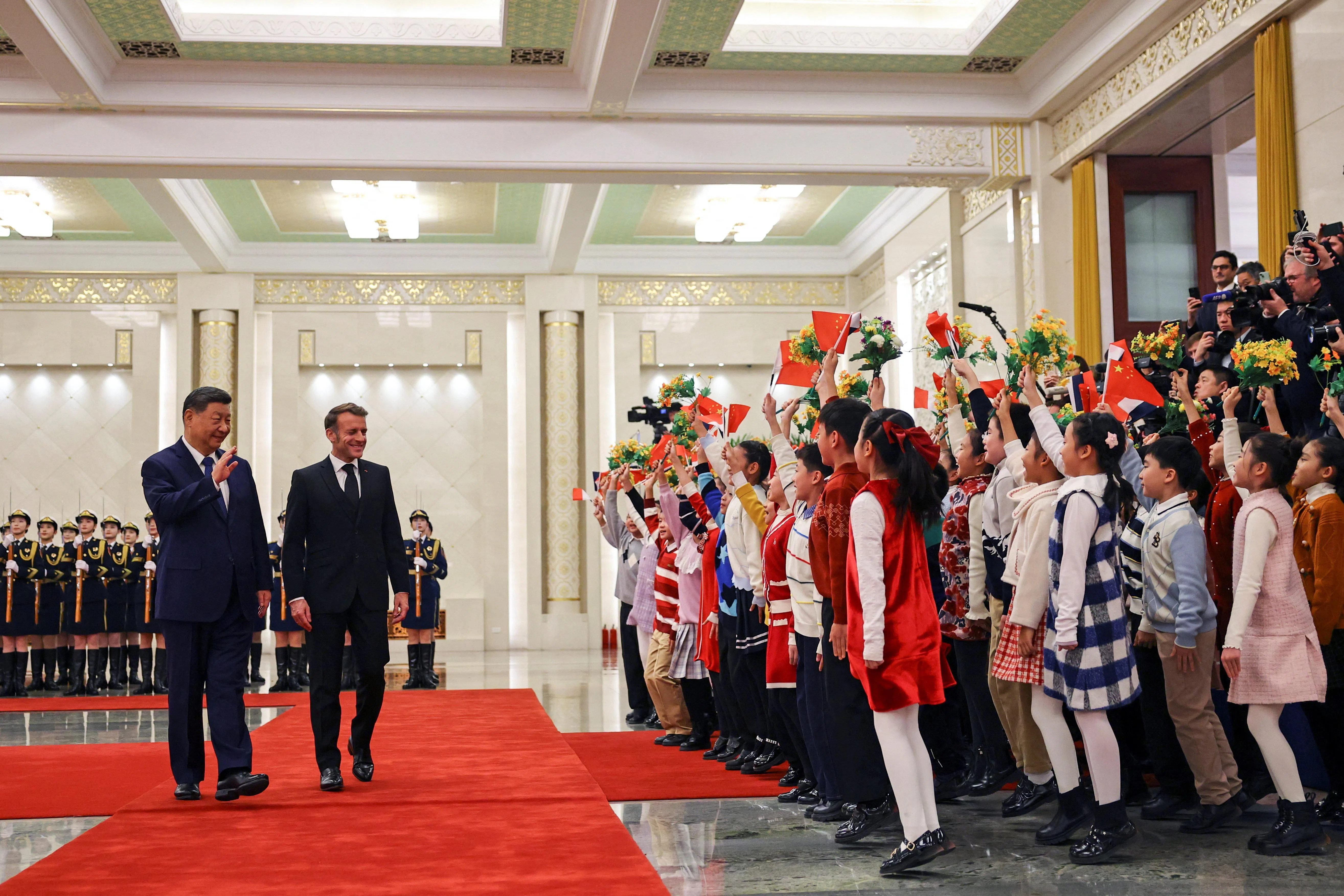 中国国家主席习近平（左）星期四（12月4日）在北京人民大会堂为赴华进行三天国事访问的法国总统马克龙举行欢迎仪式。图为两人在仪式上向挥舞中国国旗、鲜花的儿童致意。（路透社）