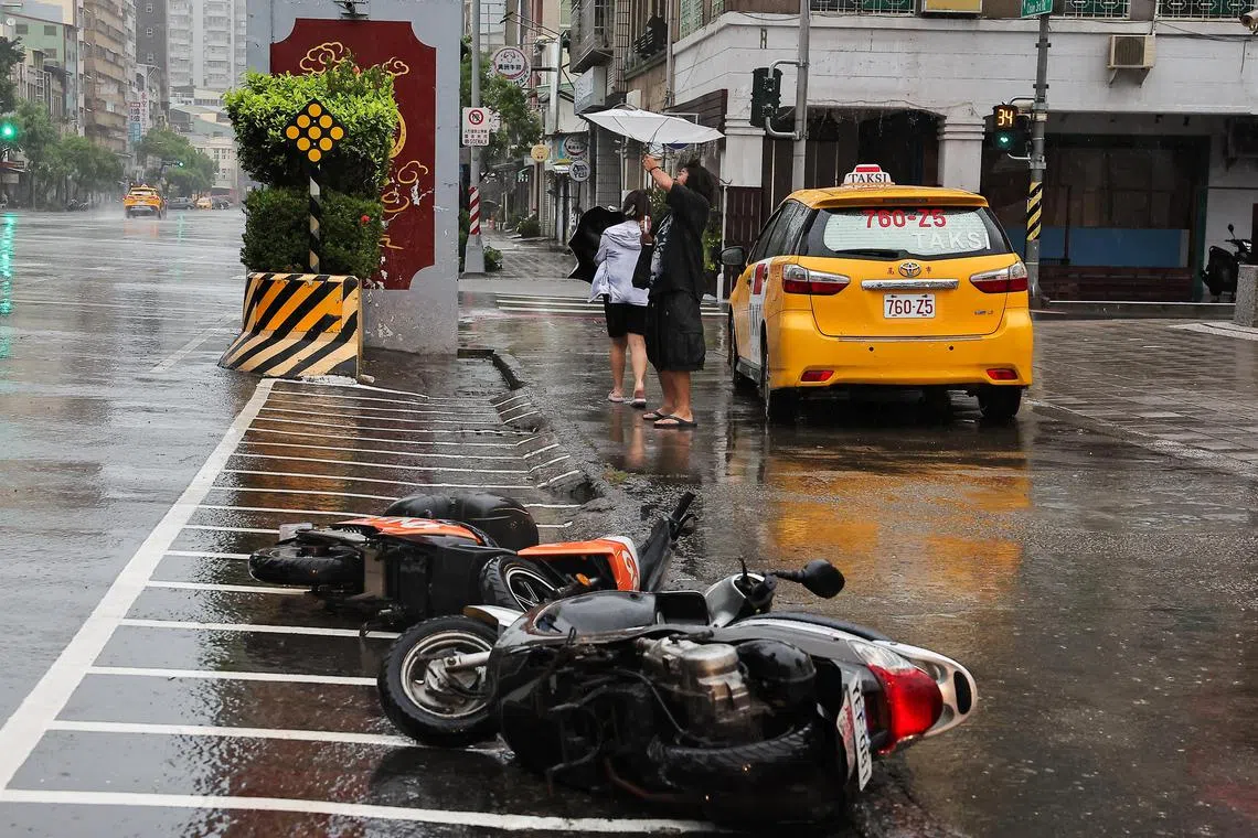 台风山陀儿逼近台湾高雄，吹倒路边电单车，行人在风雨中艰难前行。（路透社）