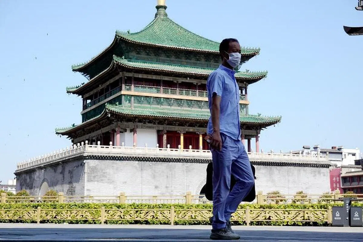 西安一位市民周三（7月6日）从钟楼前走过。周三0时起，西安全市实行7天临时性管控措施。公众娱乐休闲场所、公共文化活动场所等暂停营业一周。（中新社）