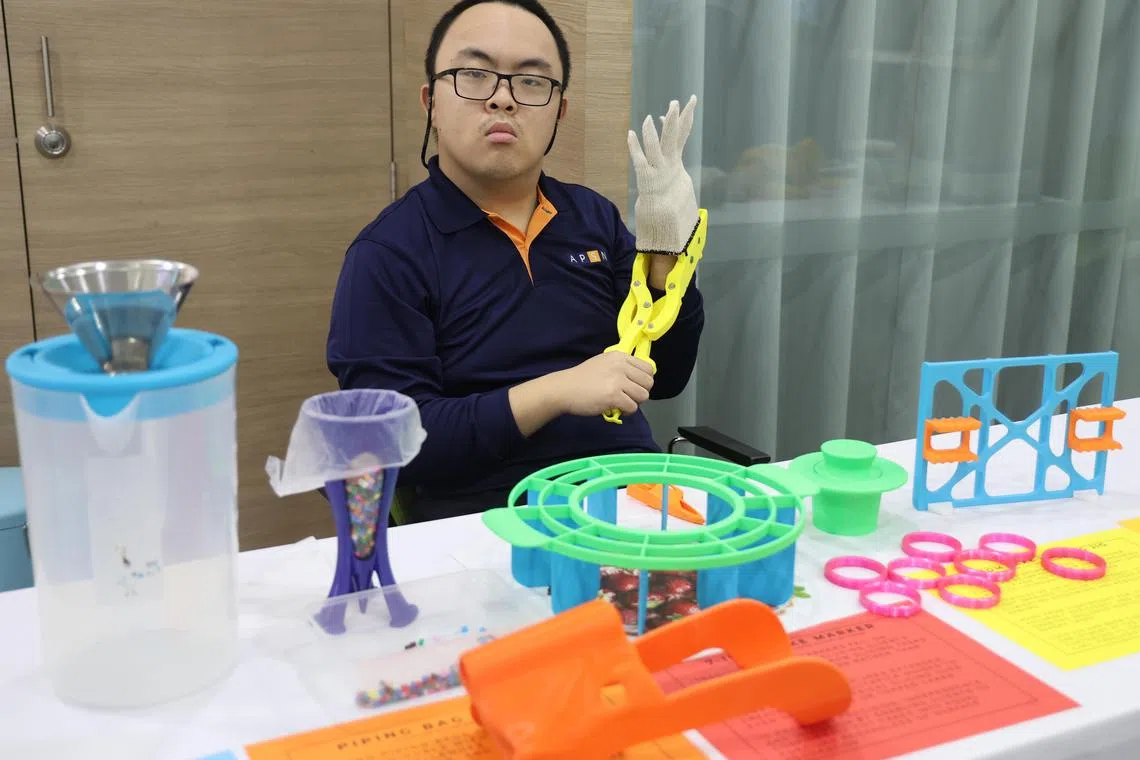 王逸峥用扩张工具帮助戴上手套。他面前放着不同尺寸的蛋糕切割模具，以及特制裱花袋撑架和防止煮咖啡时烫伤的漏斗固定器等。（邬福梁摄）