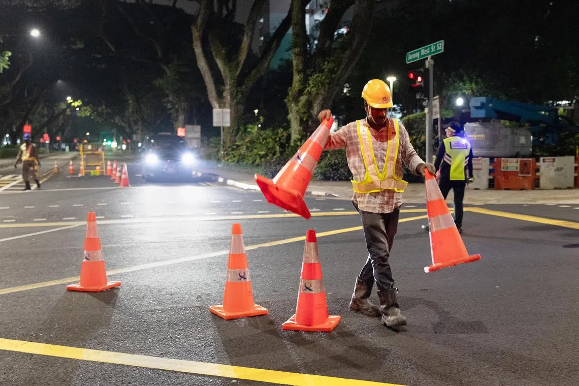 工人在裕廊西51街摆放交通锥，关闭车道，以开始施工。（蔡家增摄）