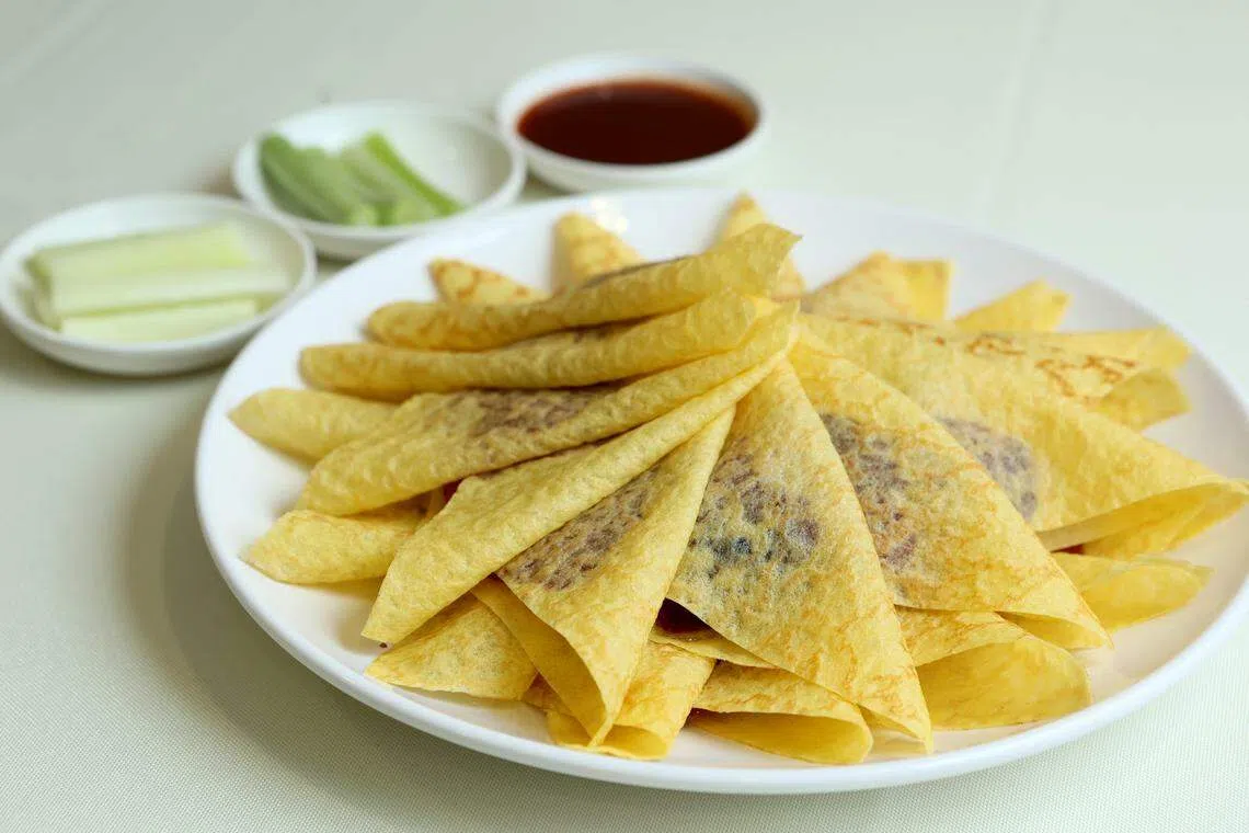 北京片皮鸭沾上甜酱，跟薄面皮、葱白和黄瓜卷着一起吃，满口留香。（龙国雄摄）