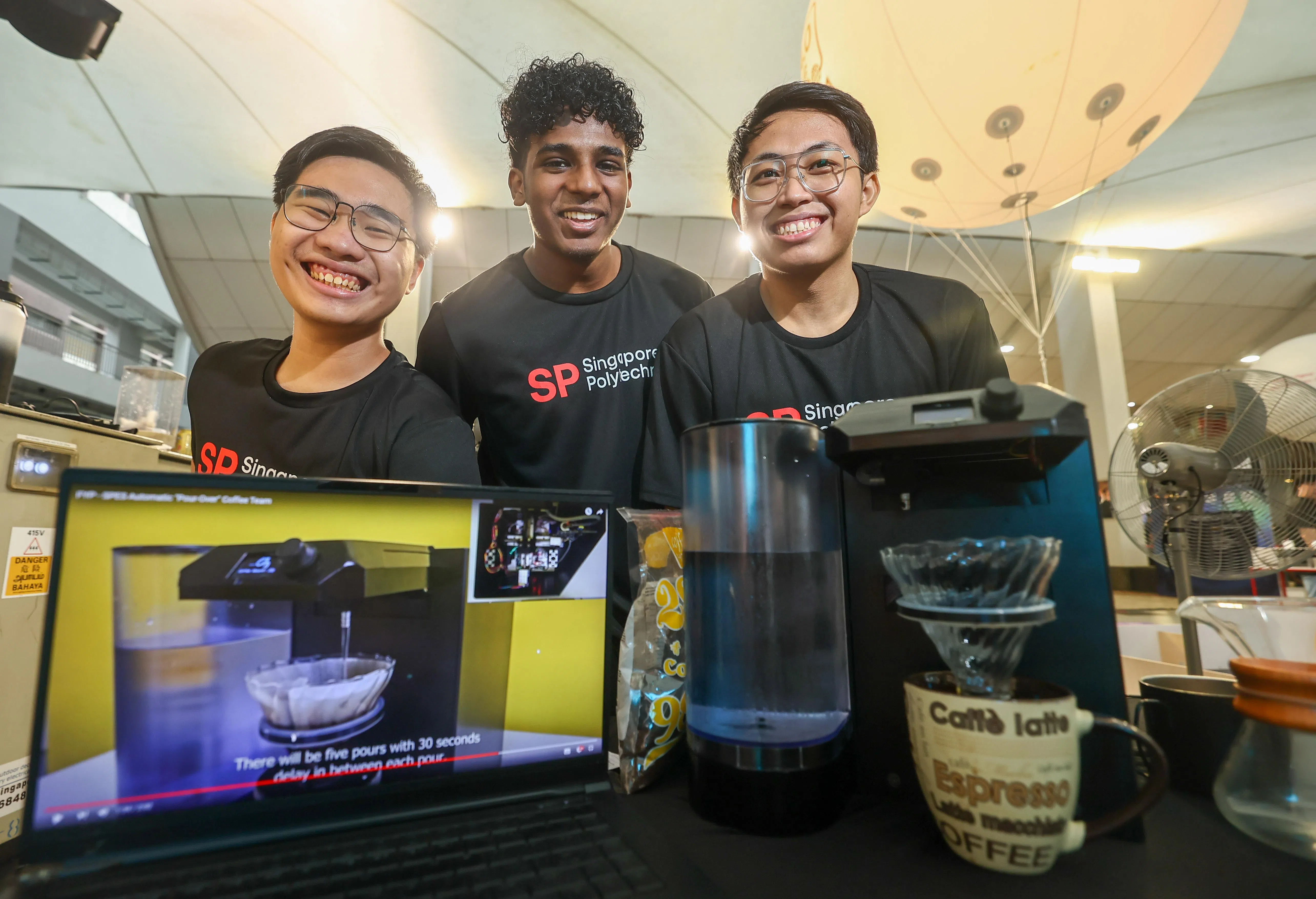 新加坡理工学院机械工程专业三年级的三名学生程文瑞（左起）、塔瓦巴和阿德里，模拟咖啡师的技艺，共同研发一款自动化的手冲咖啡机，让咖啡制作新手也能在家里喝上手冲咖啡。（陈渊庄摄）