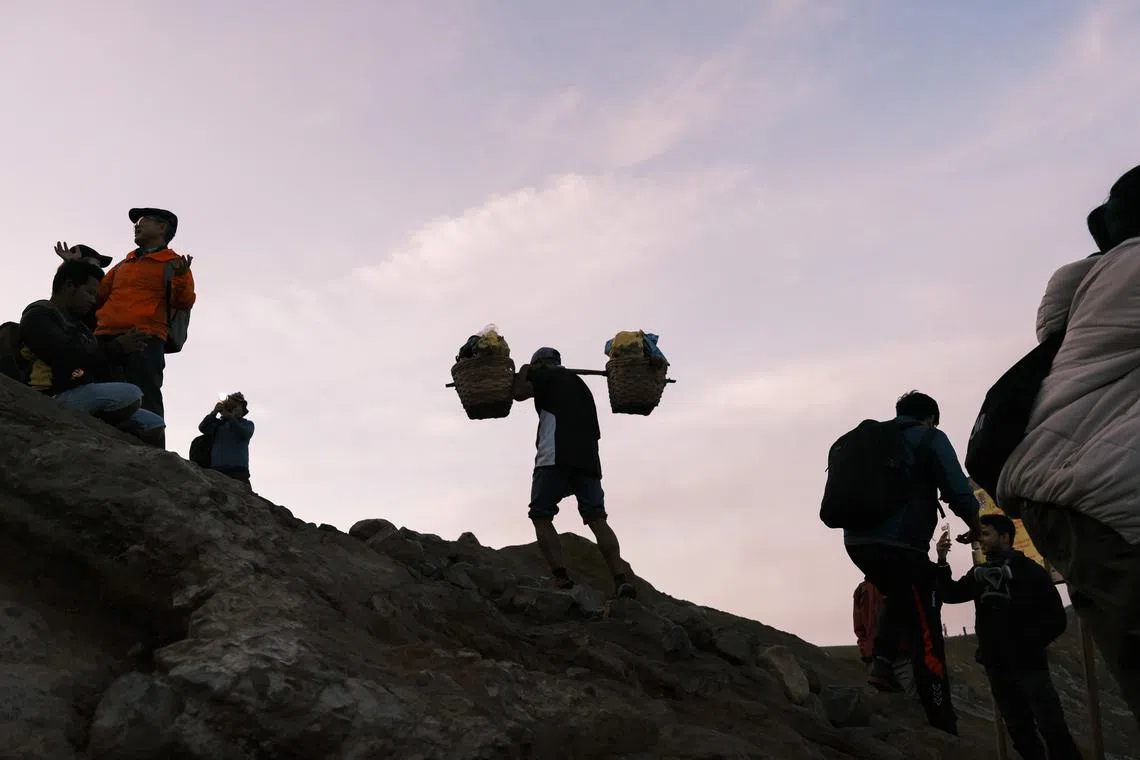 一名矿工肩挑硫磺走出火山口，周围的游客则在等待日出。（钟俊鸿摄）