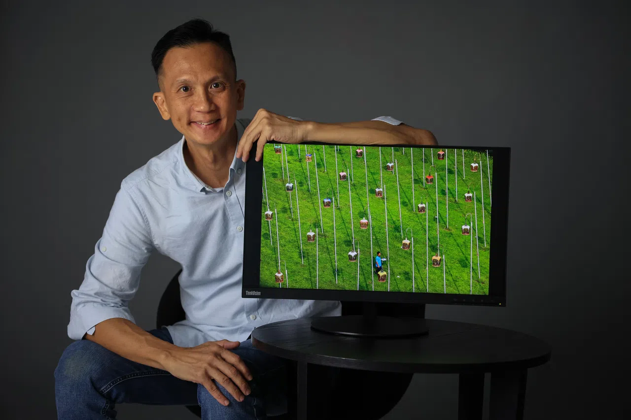 《联合早报》高级摄影记者陈斌勤没有想到赏鸟场所，会像足球场一样宽广，十分壮观。图中屏幕显示的照片，是位于义顺5道第707座组屋附近的空地，爱鸟者的聚集之处。（龙国雄摄）