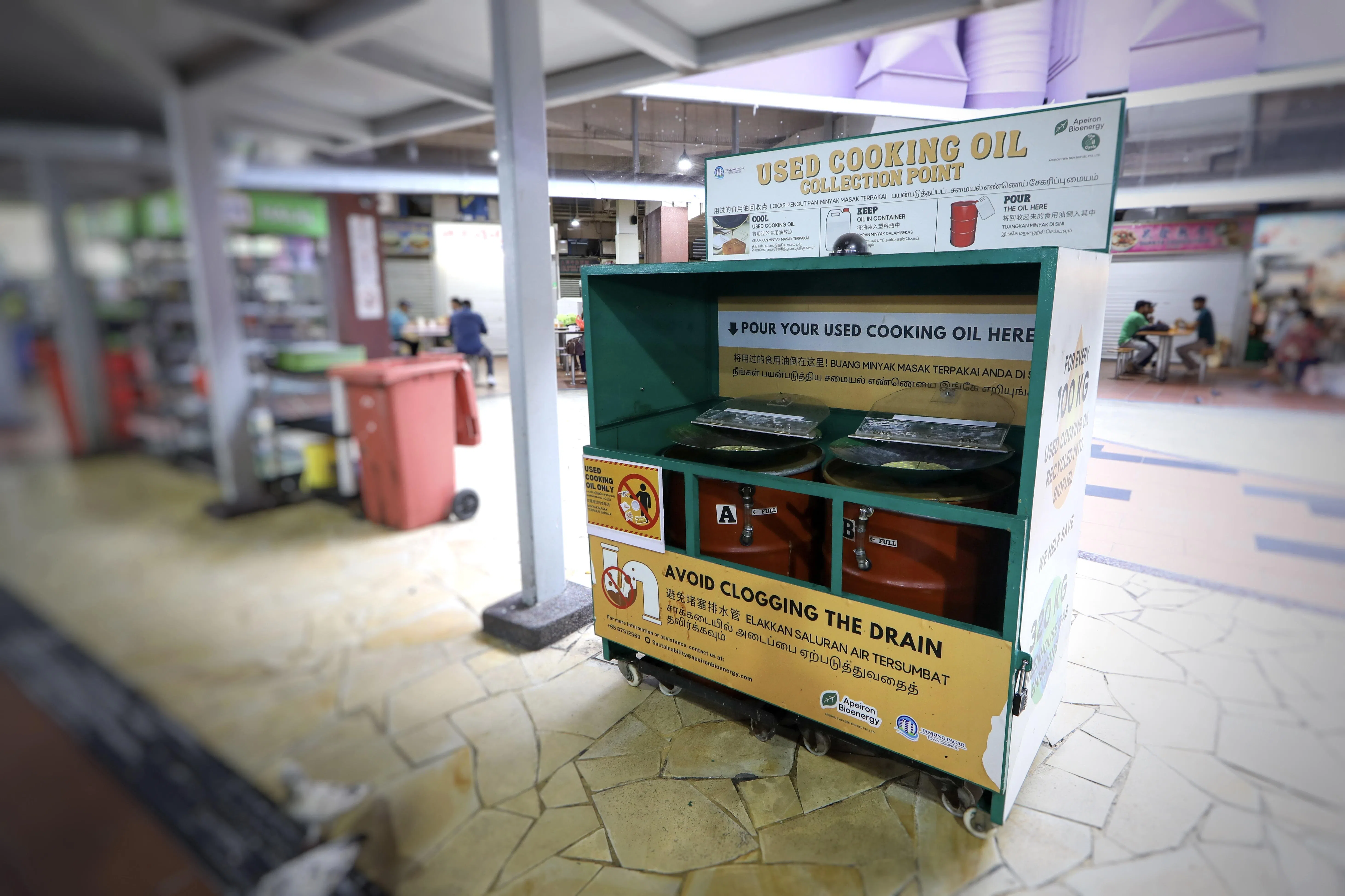 废弃食用油回收点设置在碗盘回收处旁边，方便小贩实施这项环保方案。有中文、马来文，以及淡米尔文提醒小贩将用过的食用油倒在回收点，避免处理不当造成排水管和地下道阻塞。（张恺恩摄）